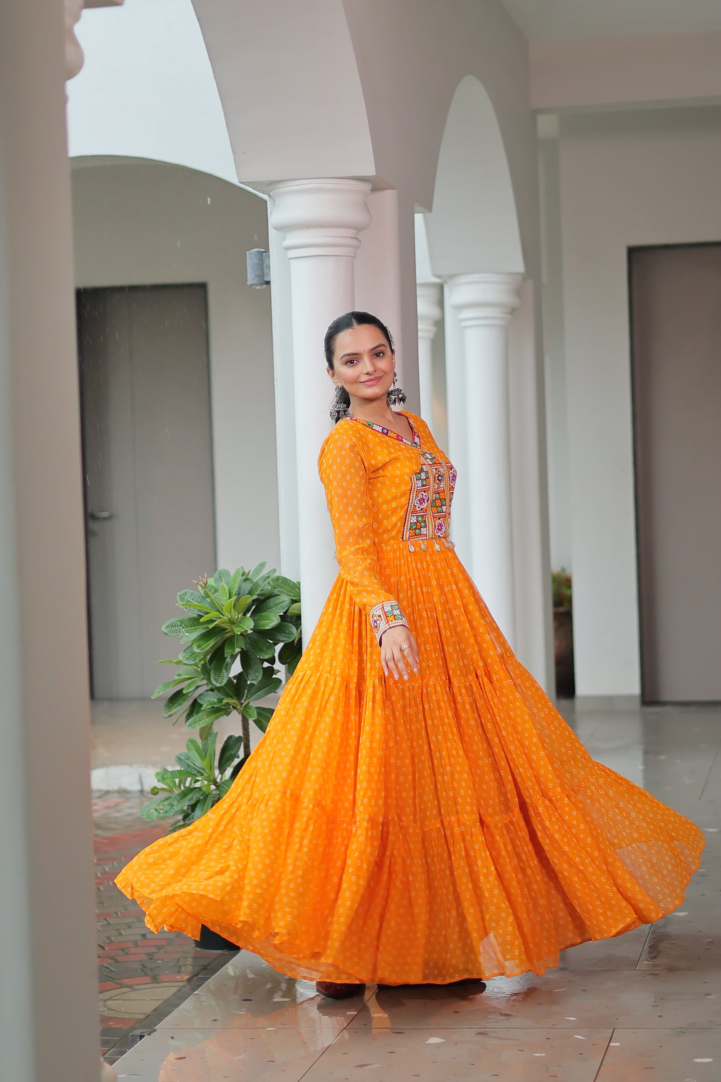 Woman in an orange saree with a floral blouse standing indoors.