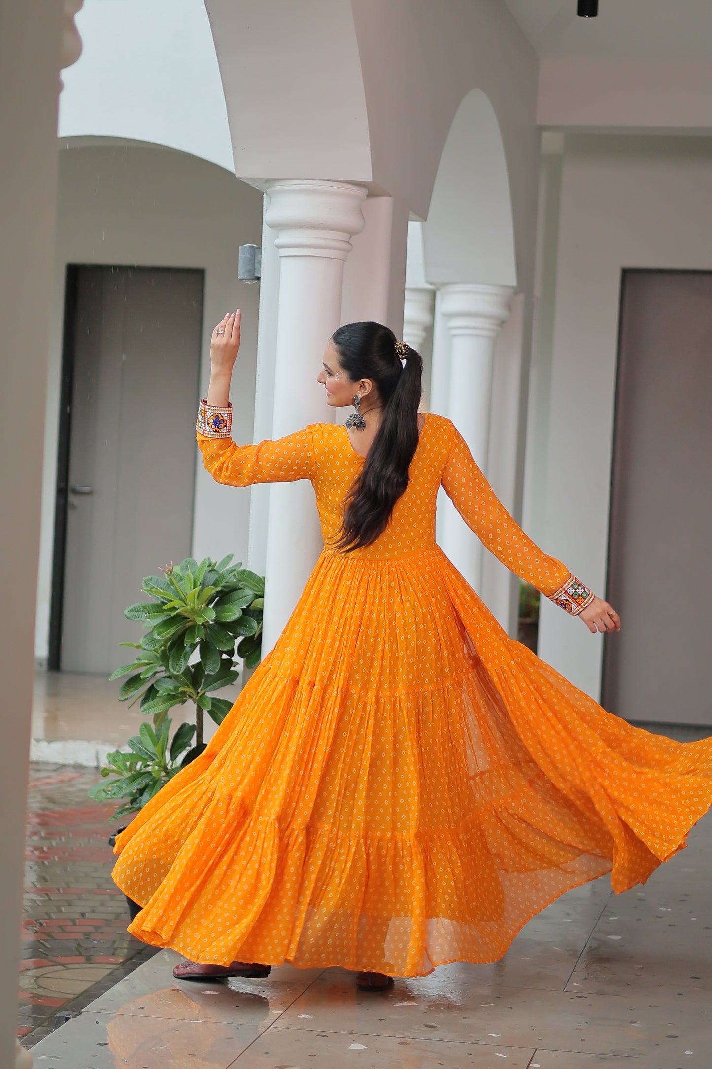 Woman in an orange dress standing on a staircase with a plant in the background