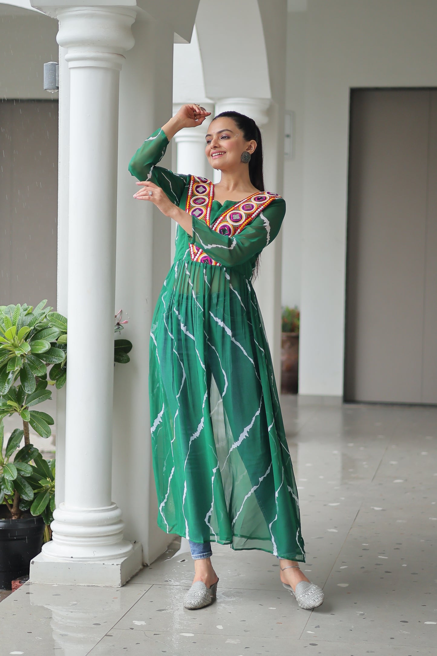 Woman in a green traditional outfit standing in front of white columns.