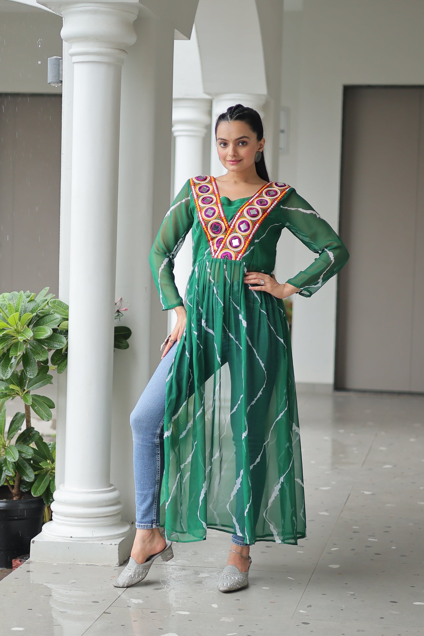 Woman in a green traditional outfit with a decorative brooch standing in a hallway.