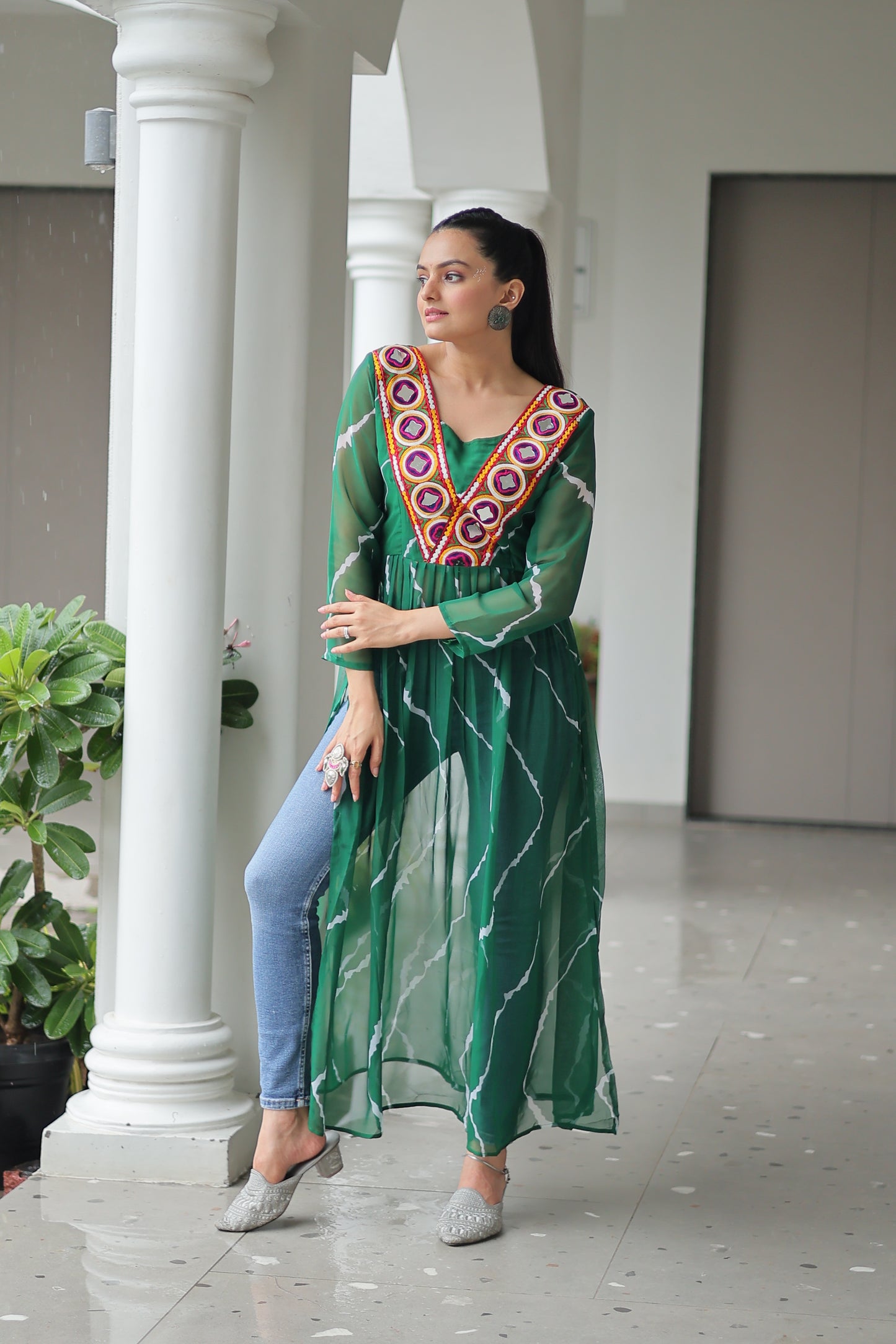 Woman in a green dress with floral patterns standing in front of a white column.
