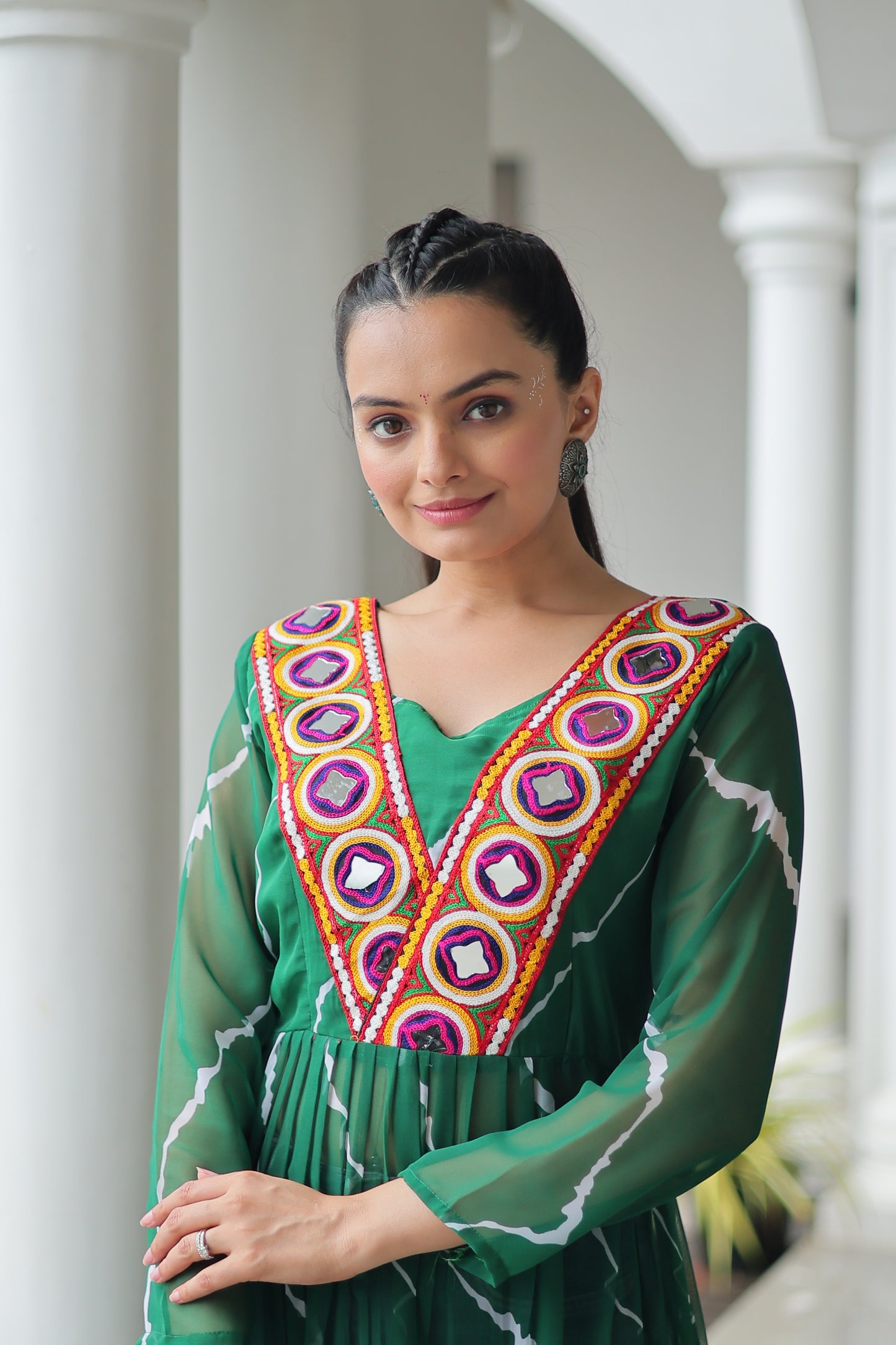 Woman wearing a green traditional outfit with colorful patterns indoors.