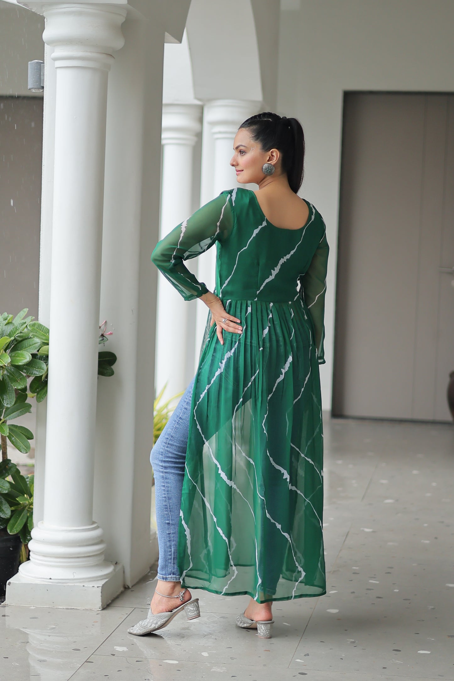 Woman in a green dress standing in a room with white columns and plants.