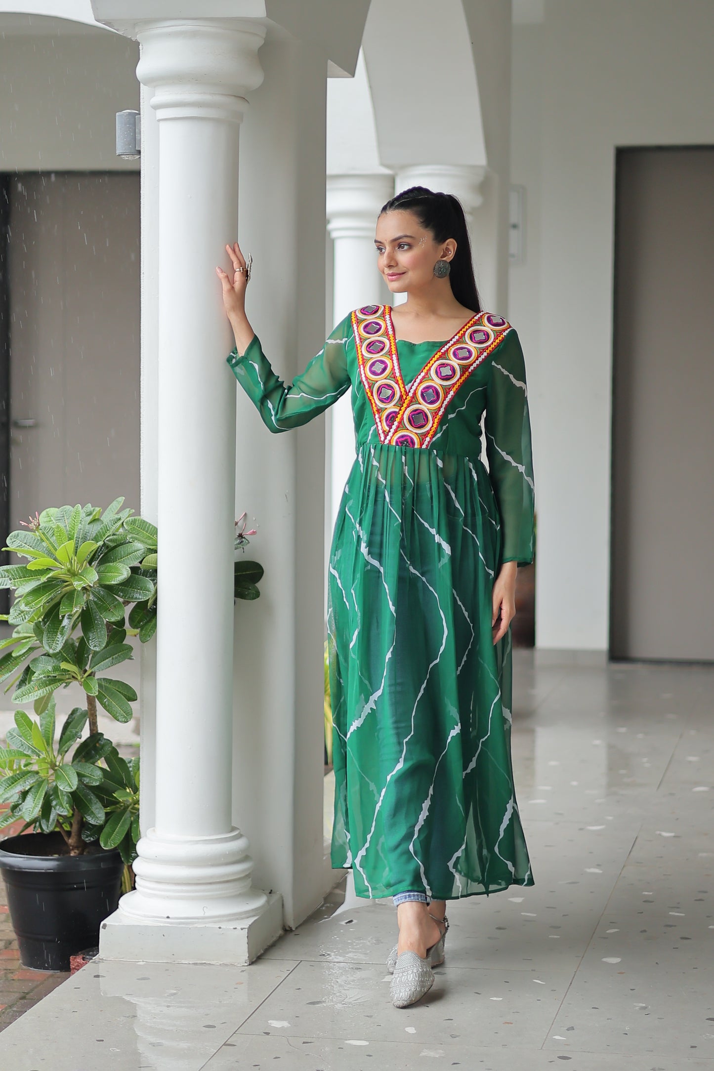 Woman in a green dress with white patterns standing in front of a mirror.