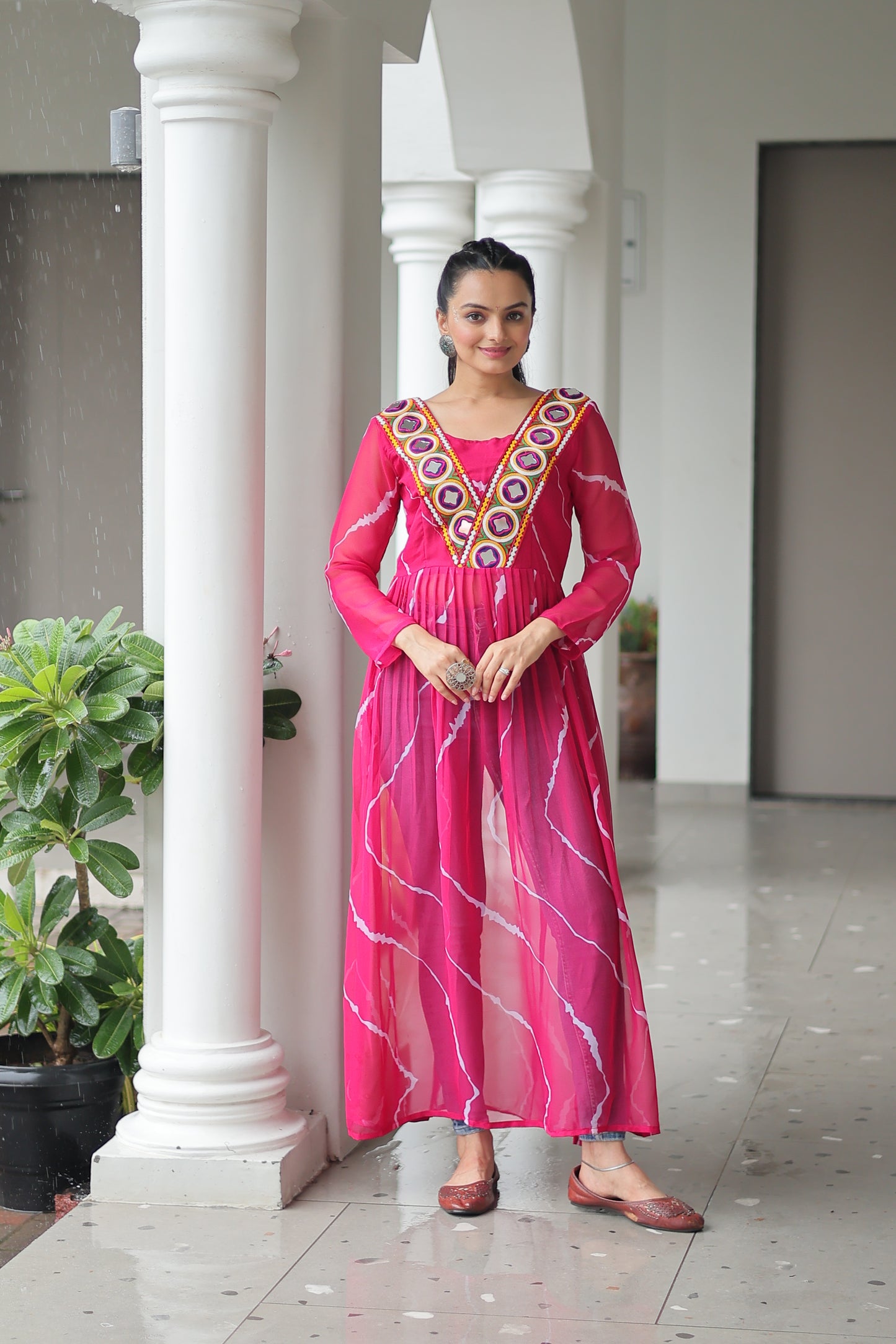 Woman in a pink traditional outfit standing in front of white columns.