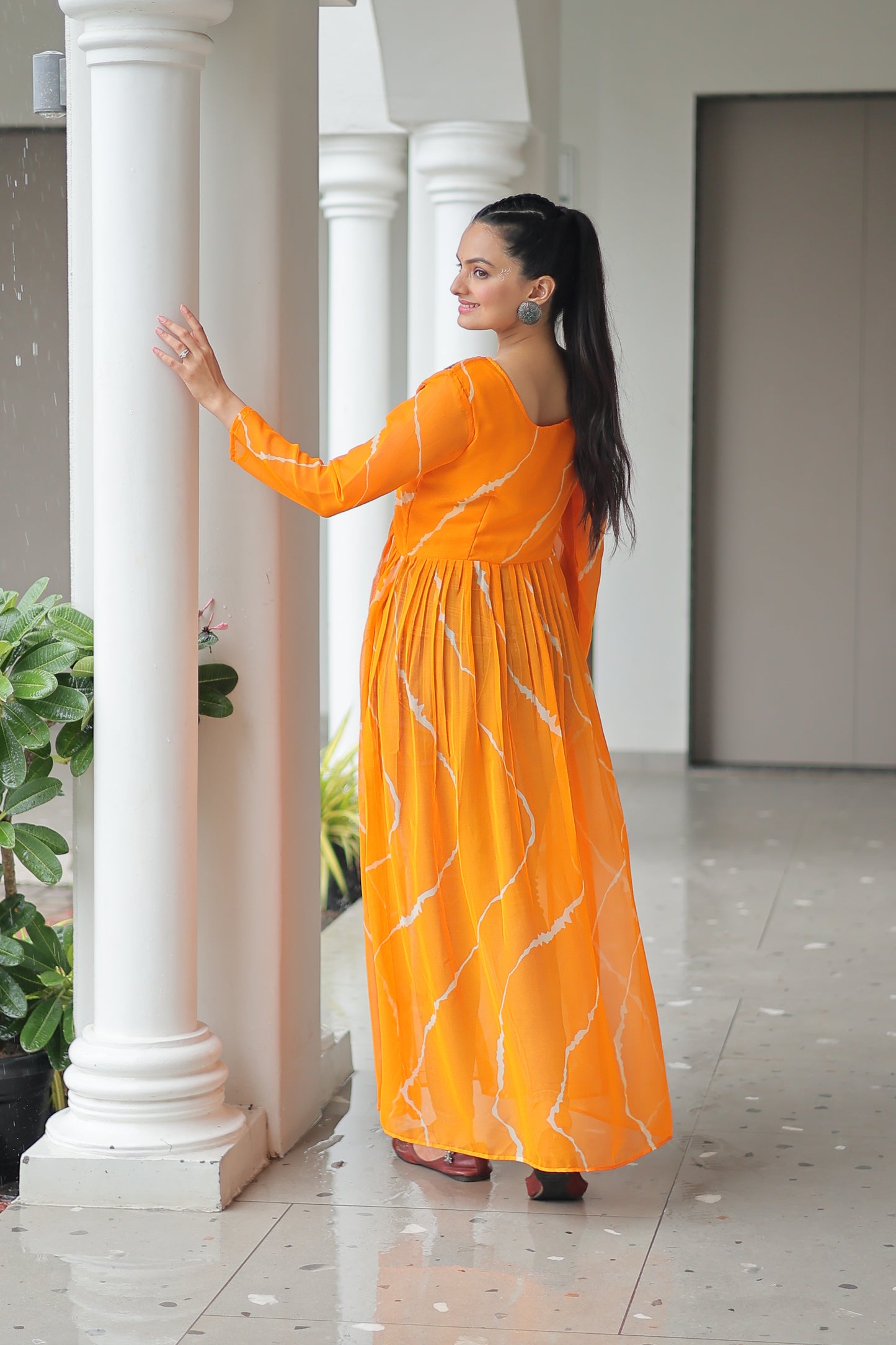 Woman in an orange dress standing in a room with white columns and green plants.