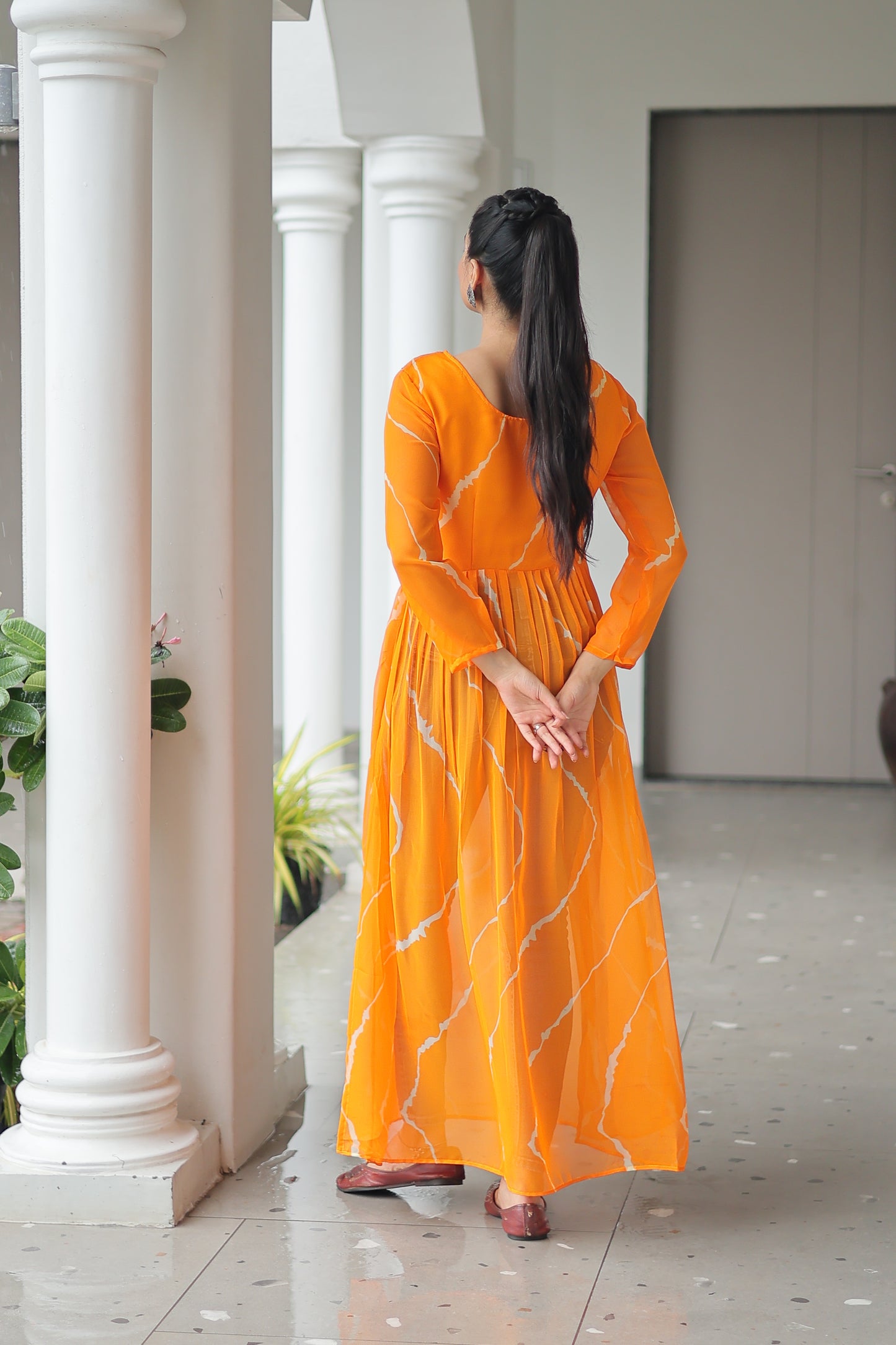 Woman in an orange saree standing indoors with white columns in the background