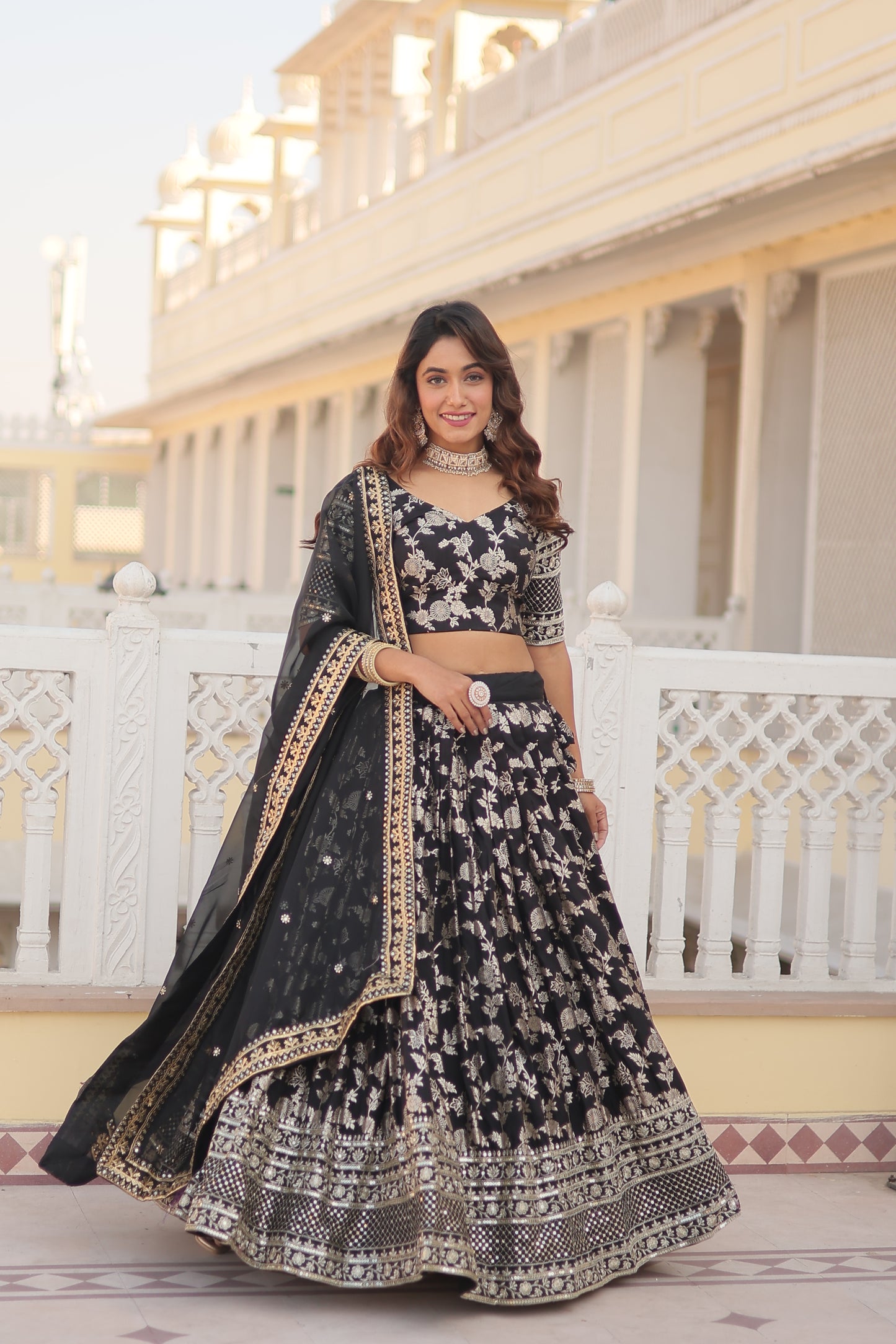 Woman in a traditional black and white embroidered outfit standing in front of a decorative wall.