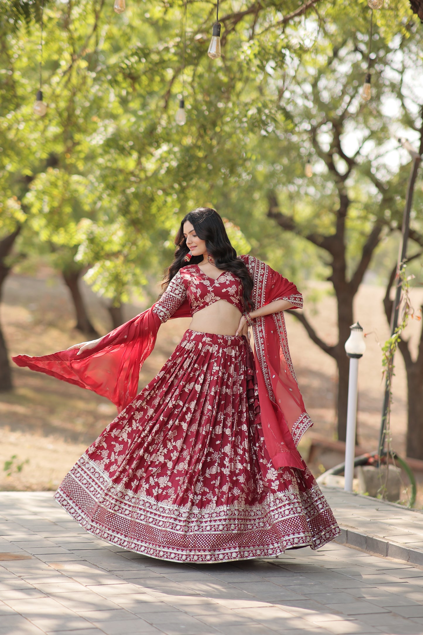Woman in a red and white traditional outfit standing against a wall with trees in the background