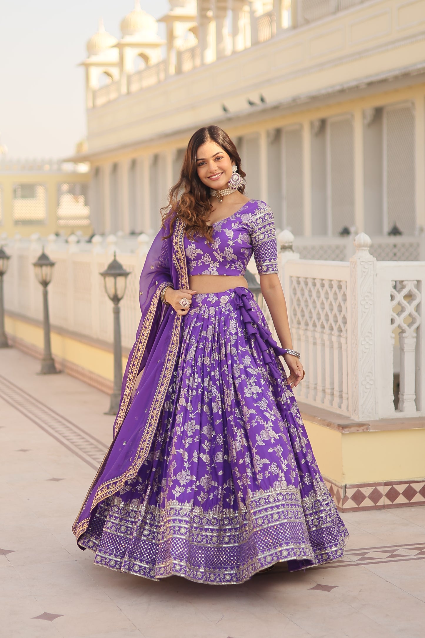 Woman in a purple traditional outfit standing in front of a building with decorative elements.