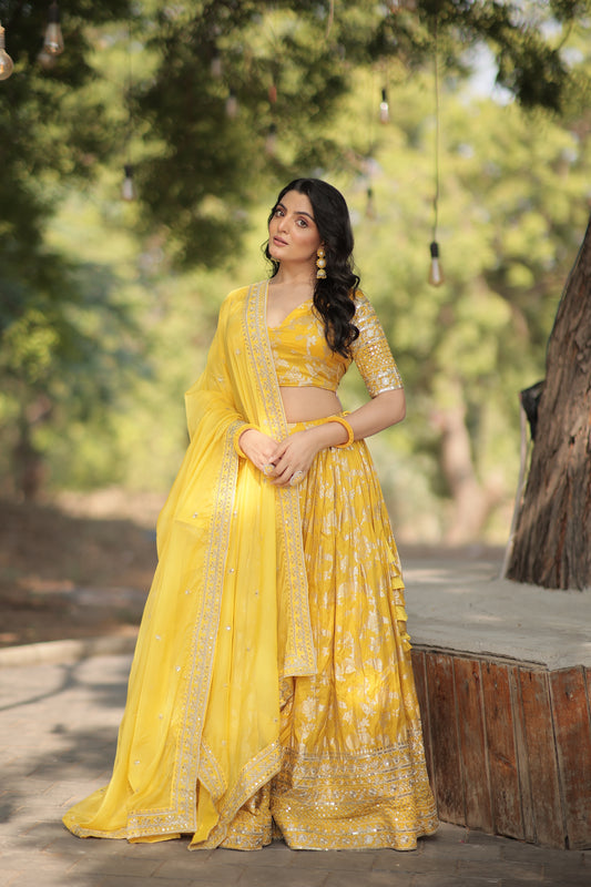 Woman in a yellow traditional outfit standing outdoors with greenery in the background