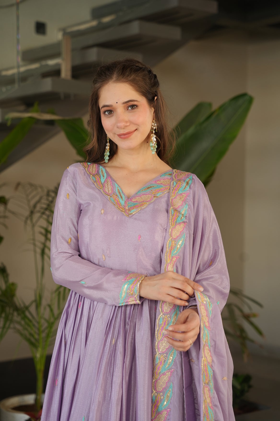 Woman in a traditional outfit with intricate designs, standing indoors.