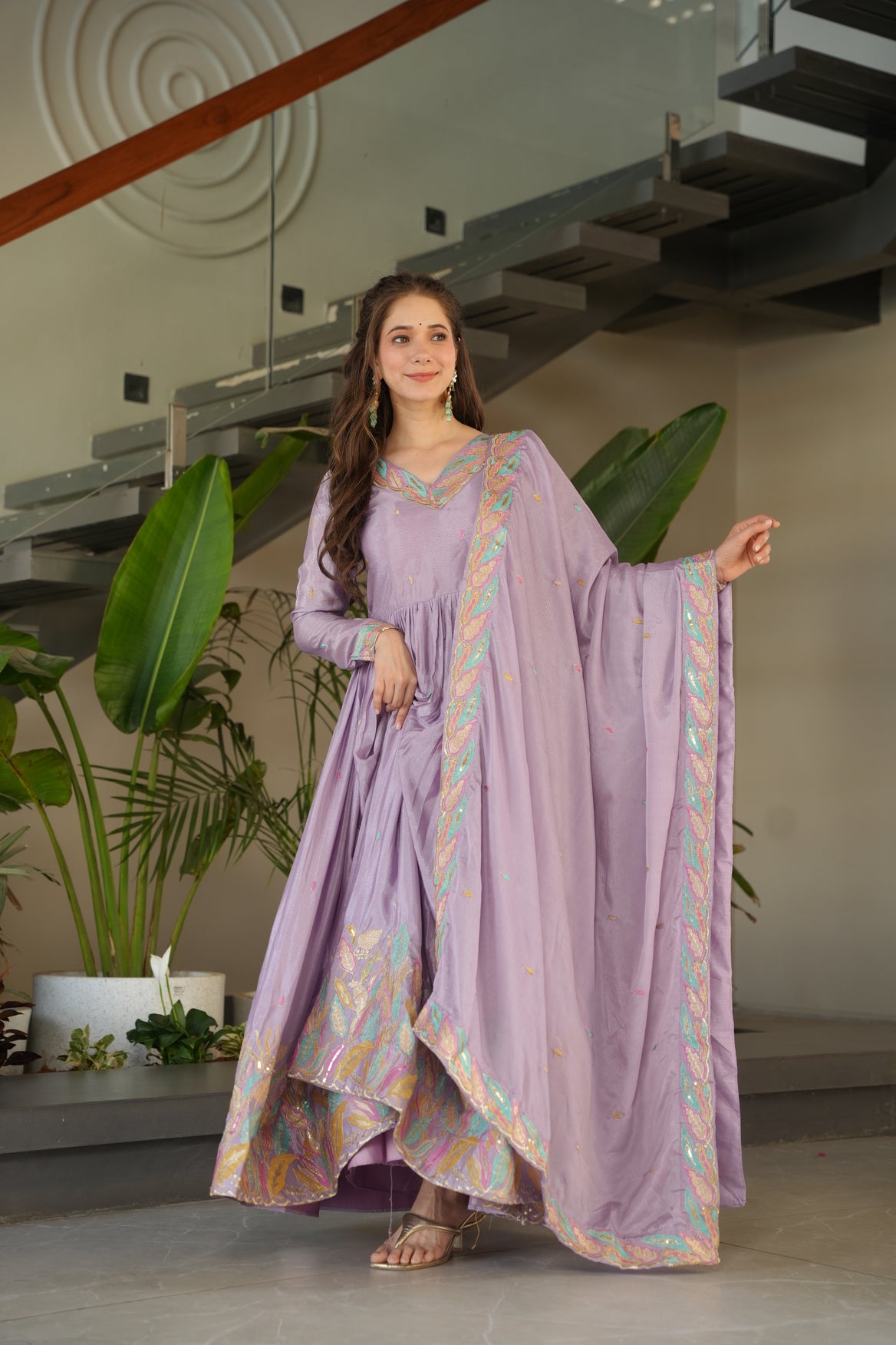 Woman wearing a long, light purple dress with decorative patterns indoors.