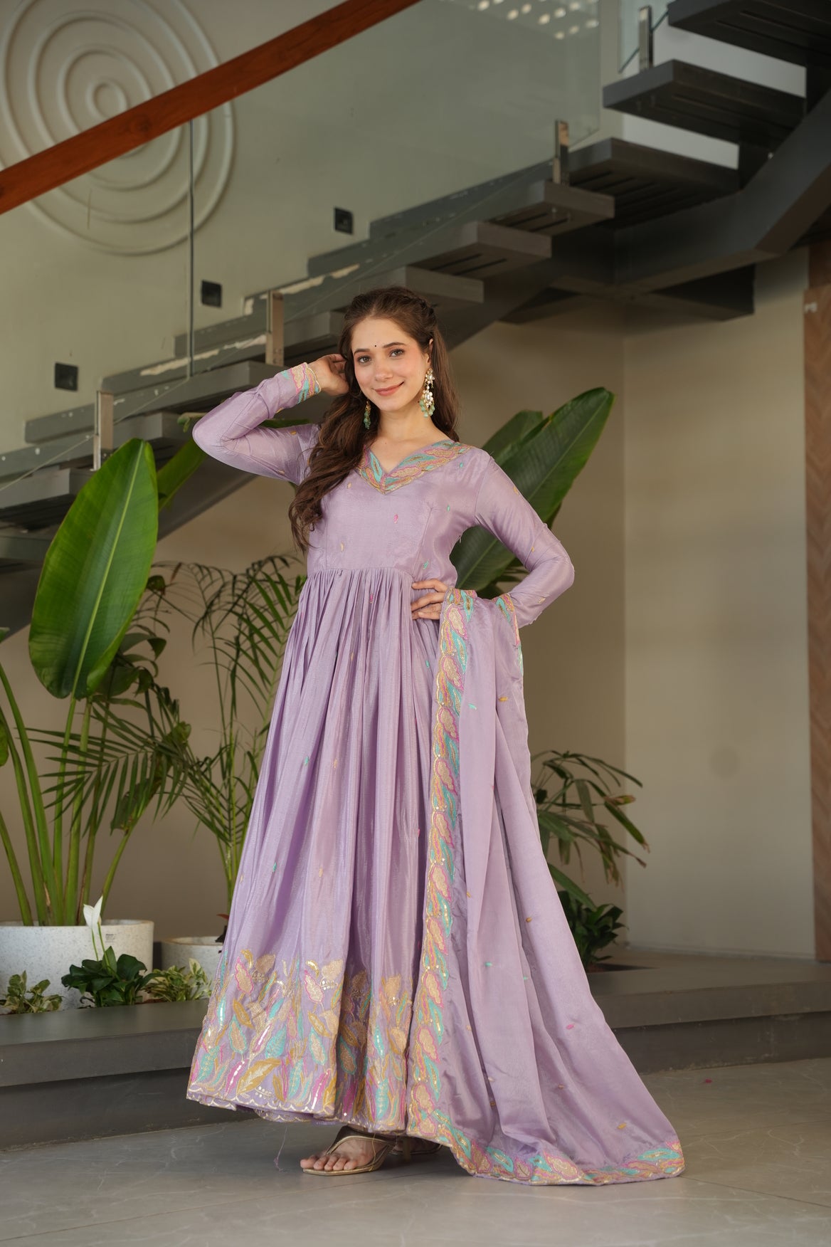 Woman in a long, light purple dress with floral patterns standing indoors.