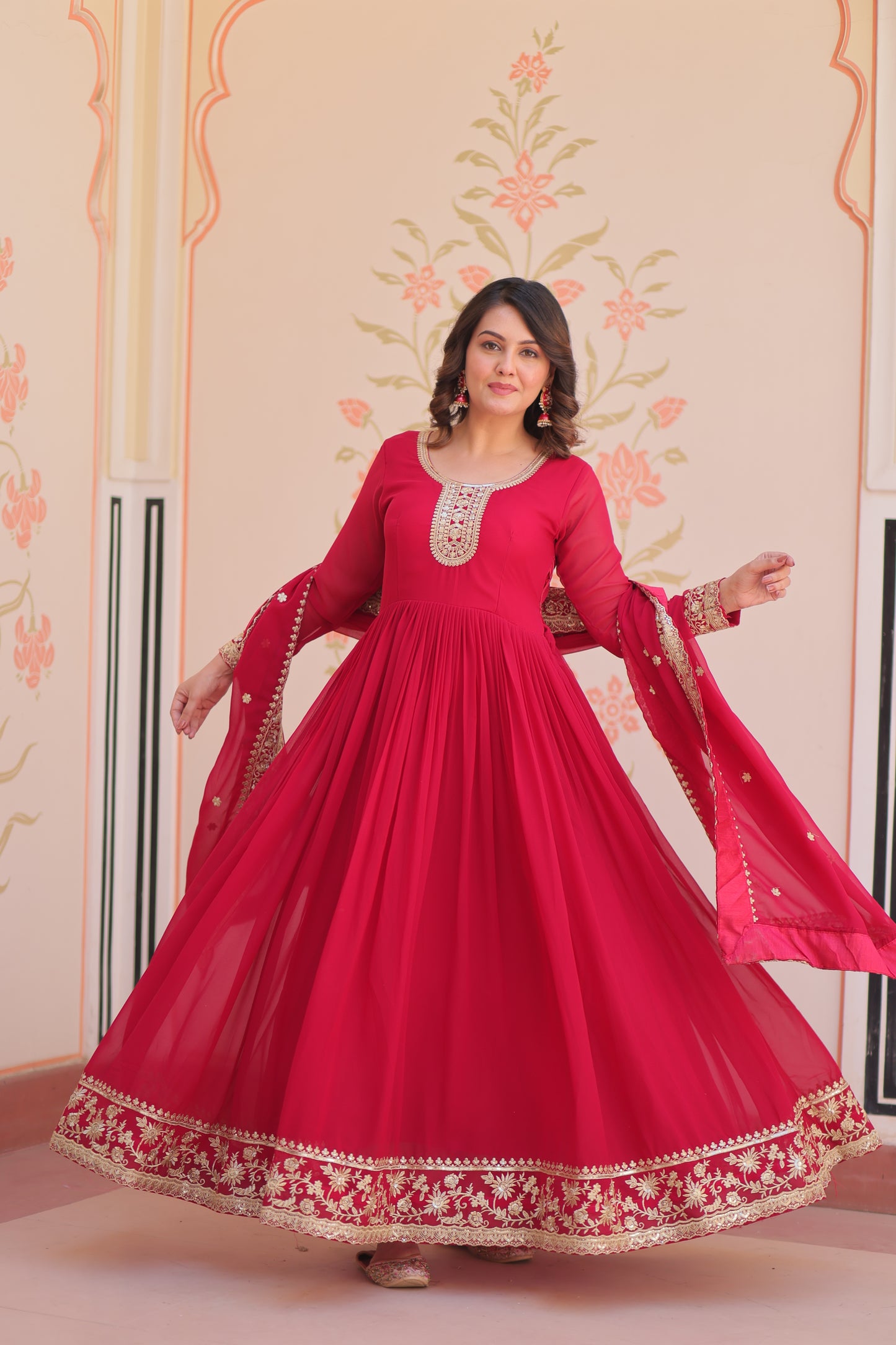 Woman wearing a red traditional outfit with intricate designs in a decorated room.