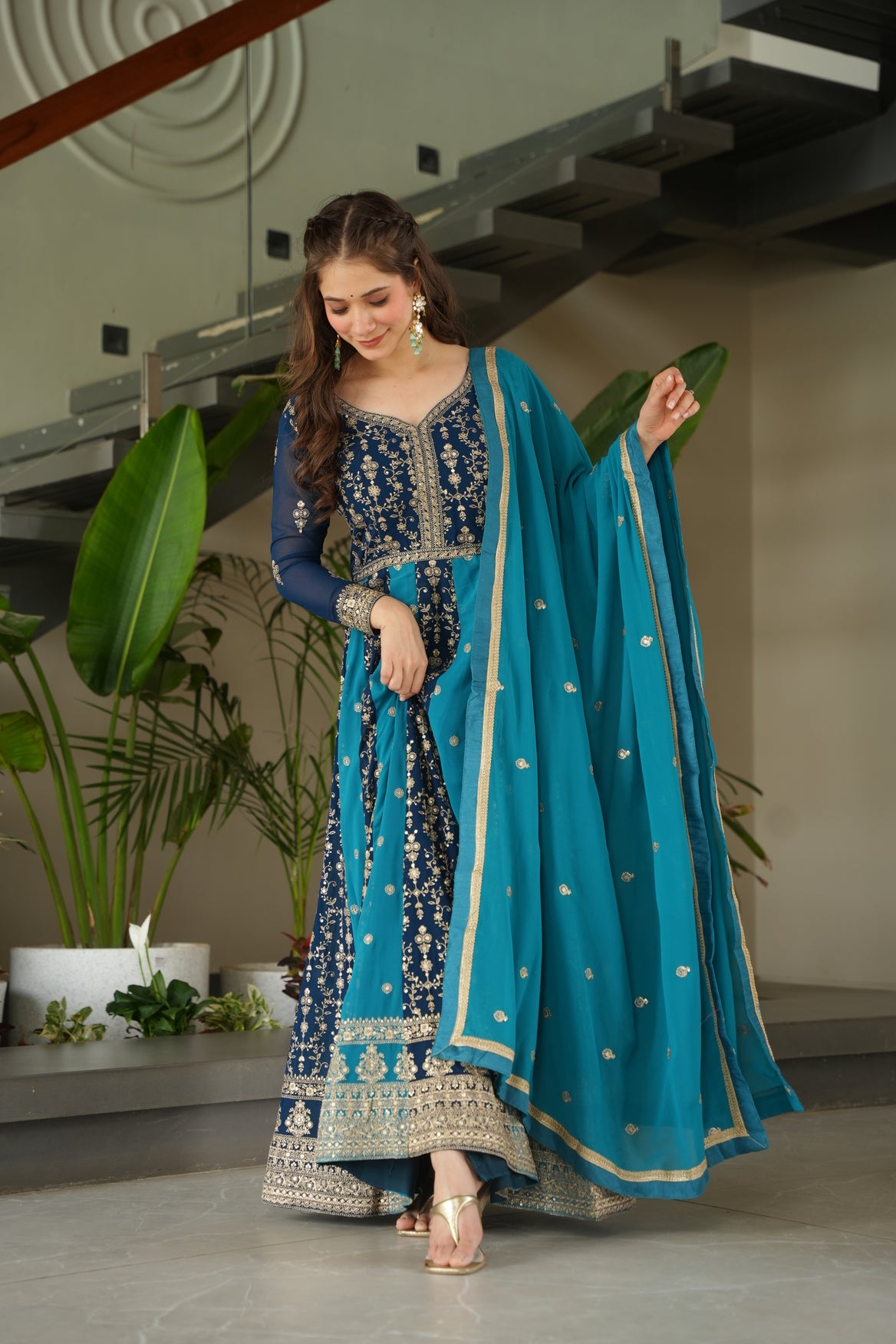 Woman in a blue traditional outfit with intricate patterns, standing indoors.