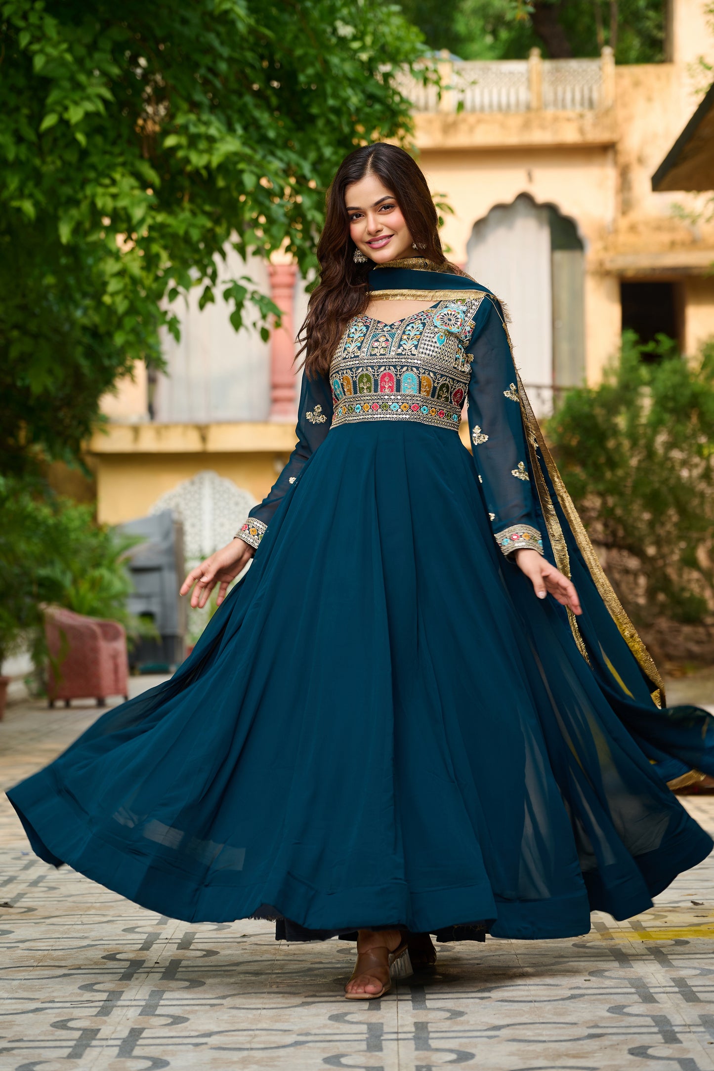 Woman in a traditional blue dress with intricate patterns standing outdoors.