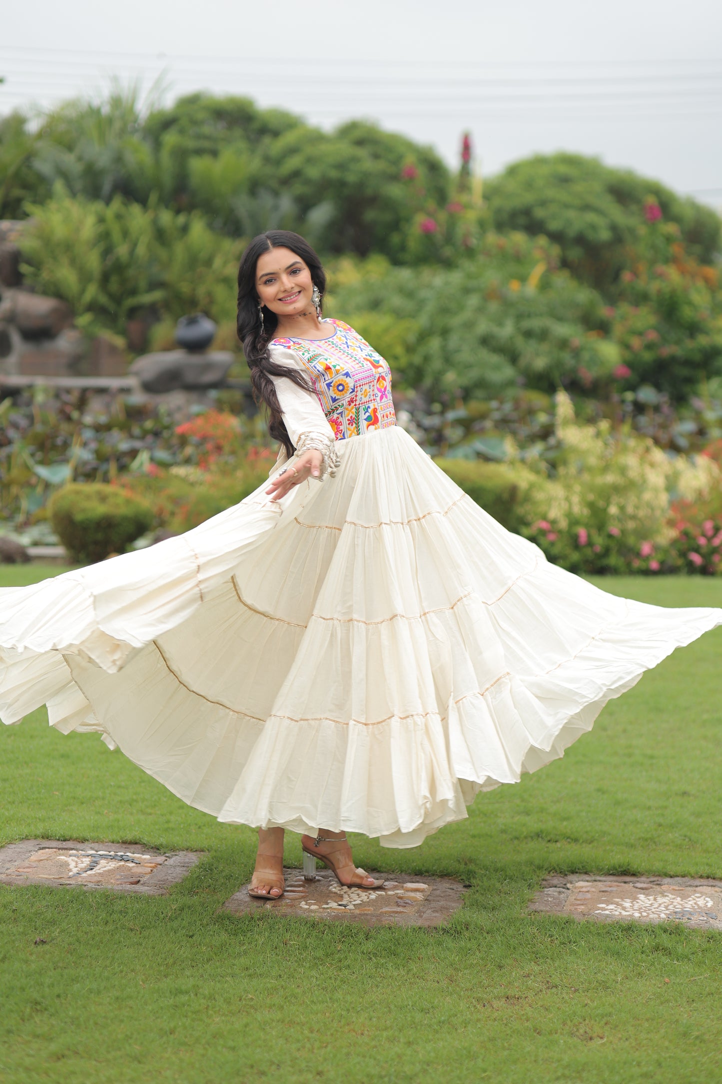 Woman in a white dress with a colorful top standing on grass with a garden background