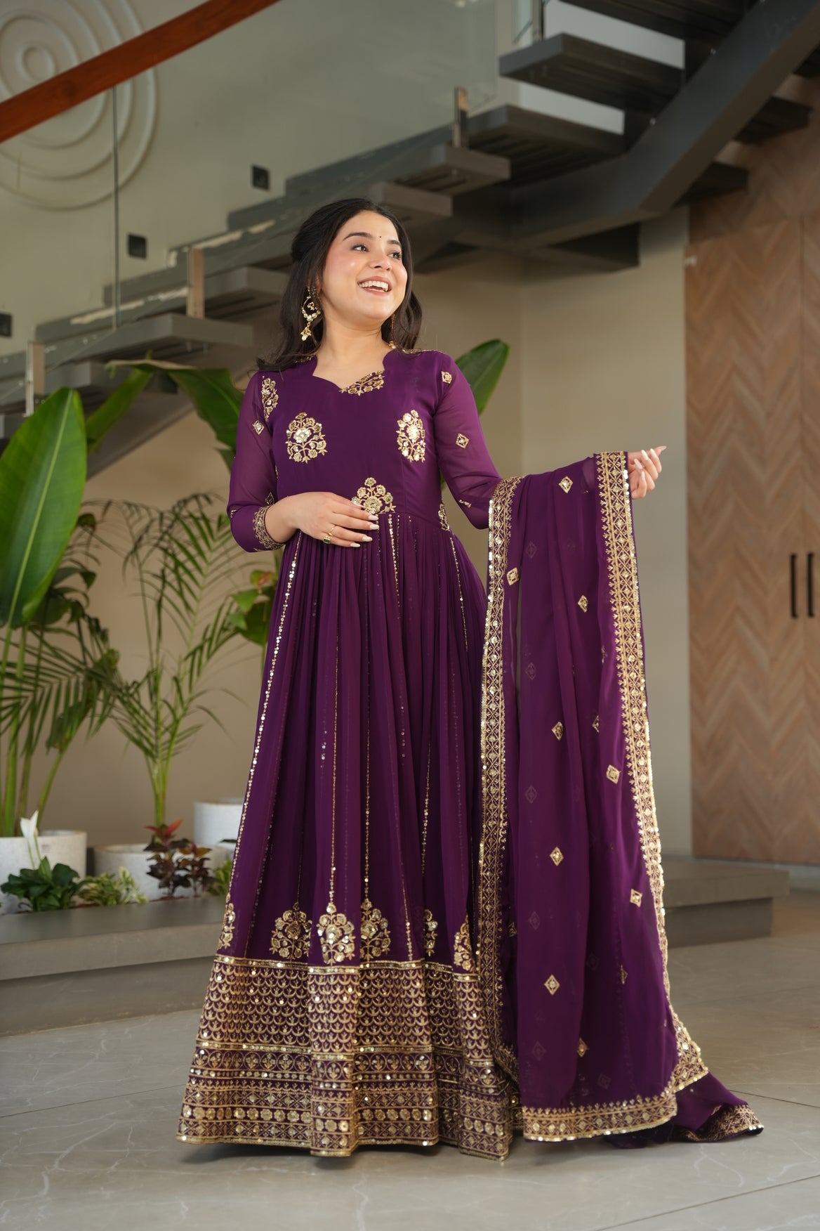 Woman in a purple traditional outfit with gold details standing indoors.