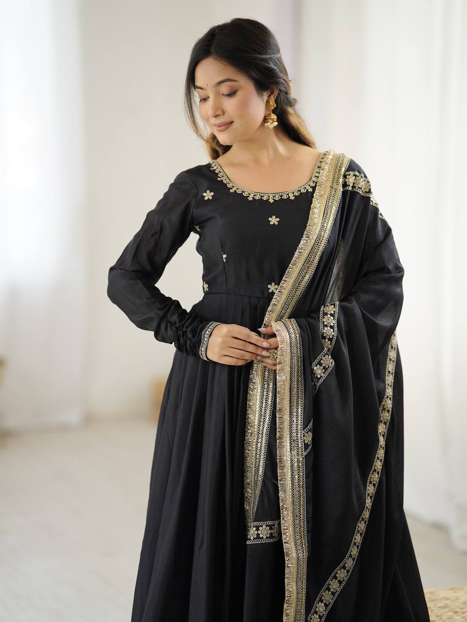 Woman wearing a black traditional outfit with gold embroidery against a white curtain background