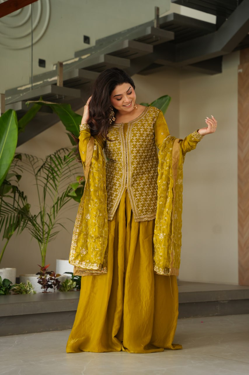 Woman in a yellow traditional outfit with intricate patterns standing indoors.