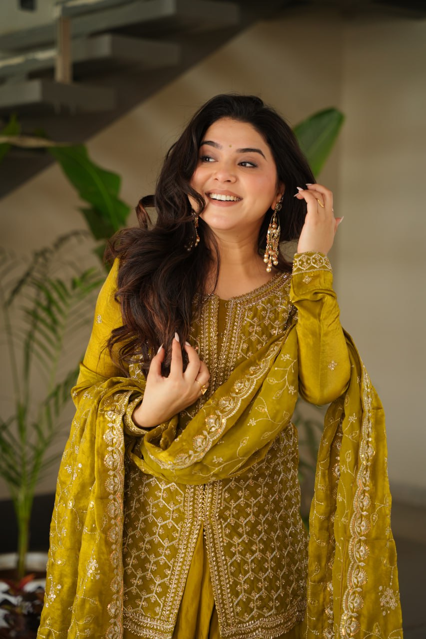 Woman in a yellow traditional outfit with intricate patterns, standing indoors.
