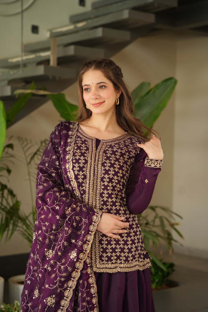 Woman in a traditional purple and gold outfit with a floral pattern, standing indoors.