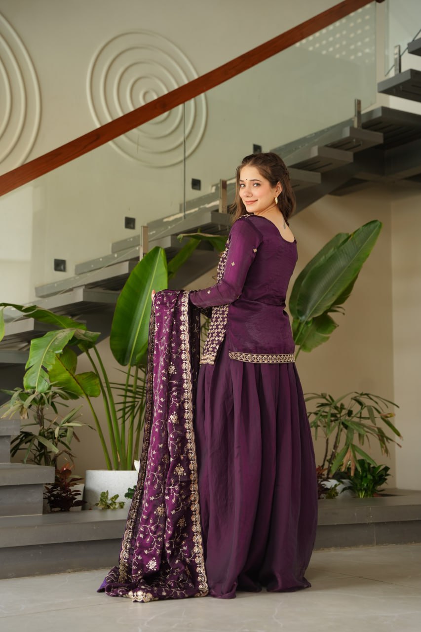 Woman in a purple traditional outfit standing in a modern indoor setting with plants.