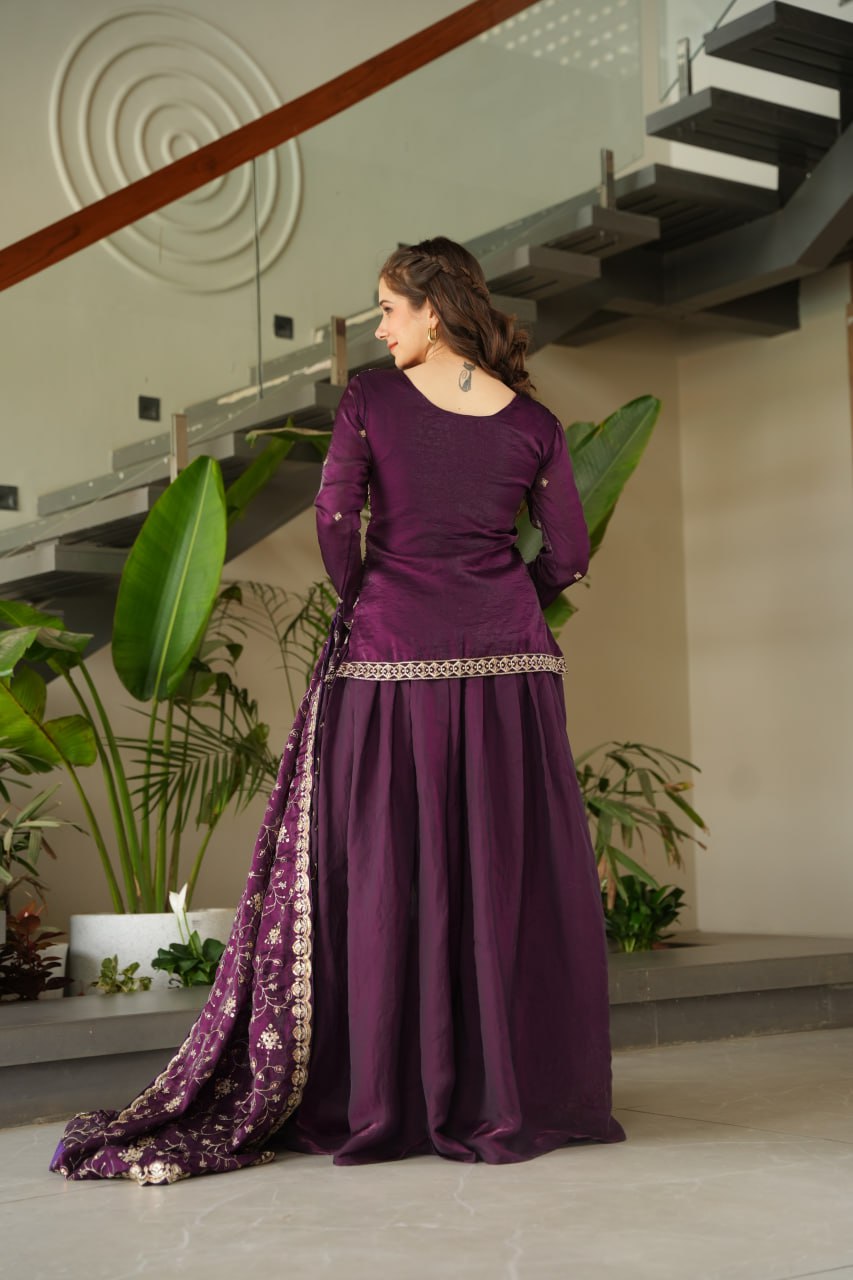 Woman in a purple traditional outfit standing indoors with plants in the background