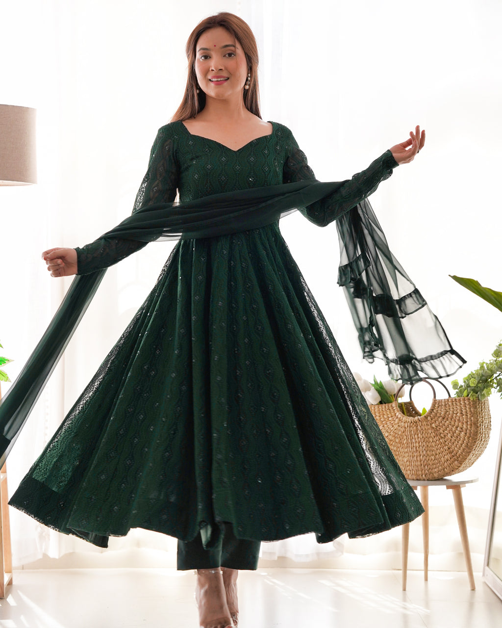 Woman wearing a green dress with sheer sleeves in a room setting.