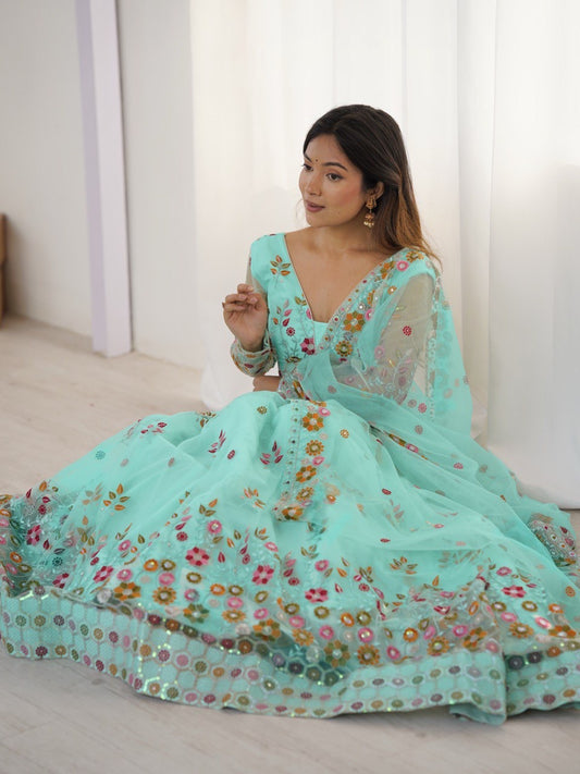 Woman wearing a light blue embroidered dress sitting on a white floor.