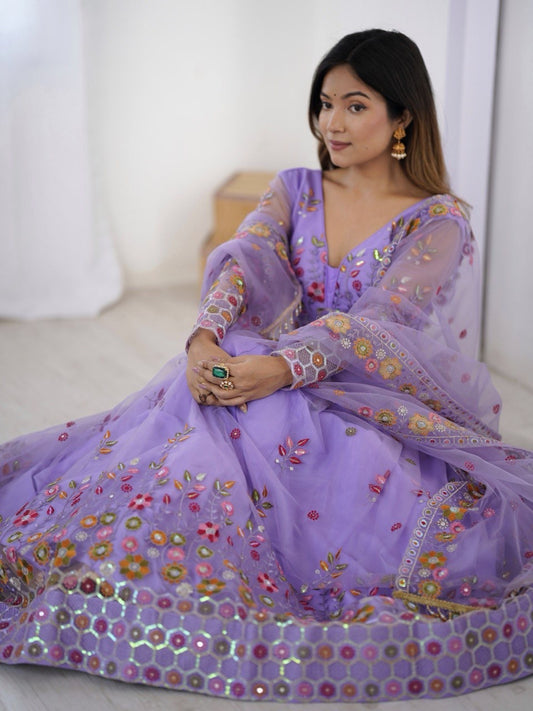 Woman wearing a purple embroidered traditional outfit sitting on a white couch.