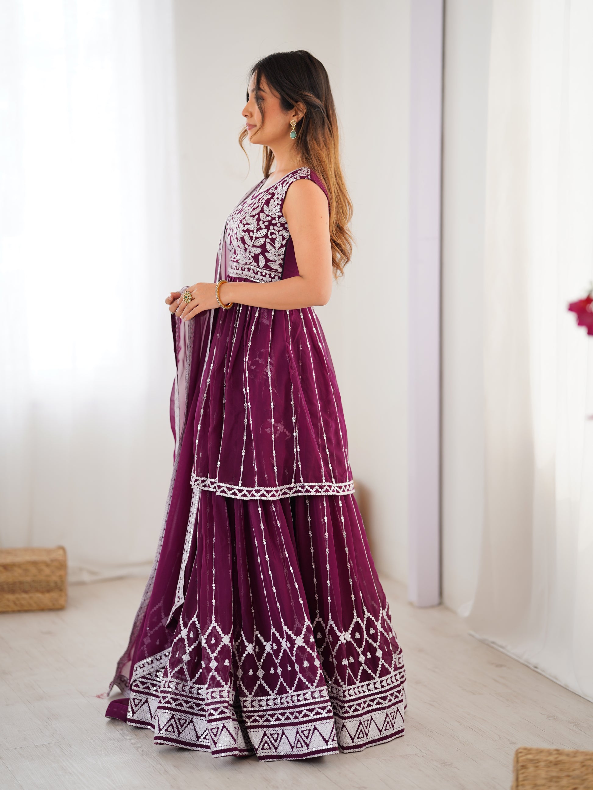 Woman wearing a long purple dress with white patterns in a minimal indoor setting.