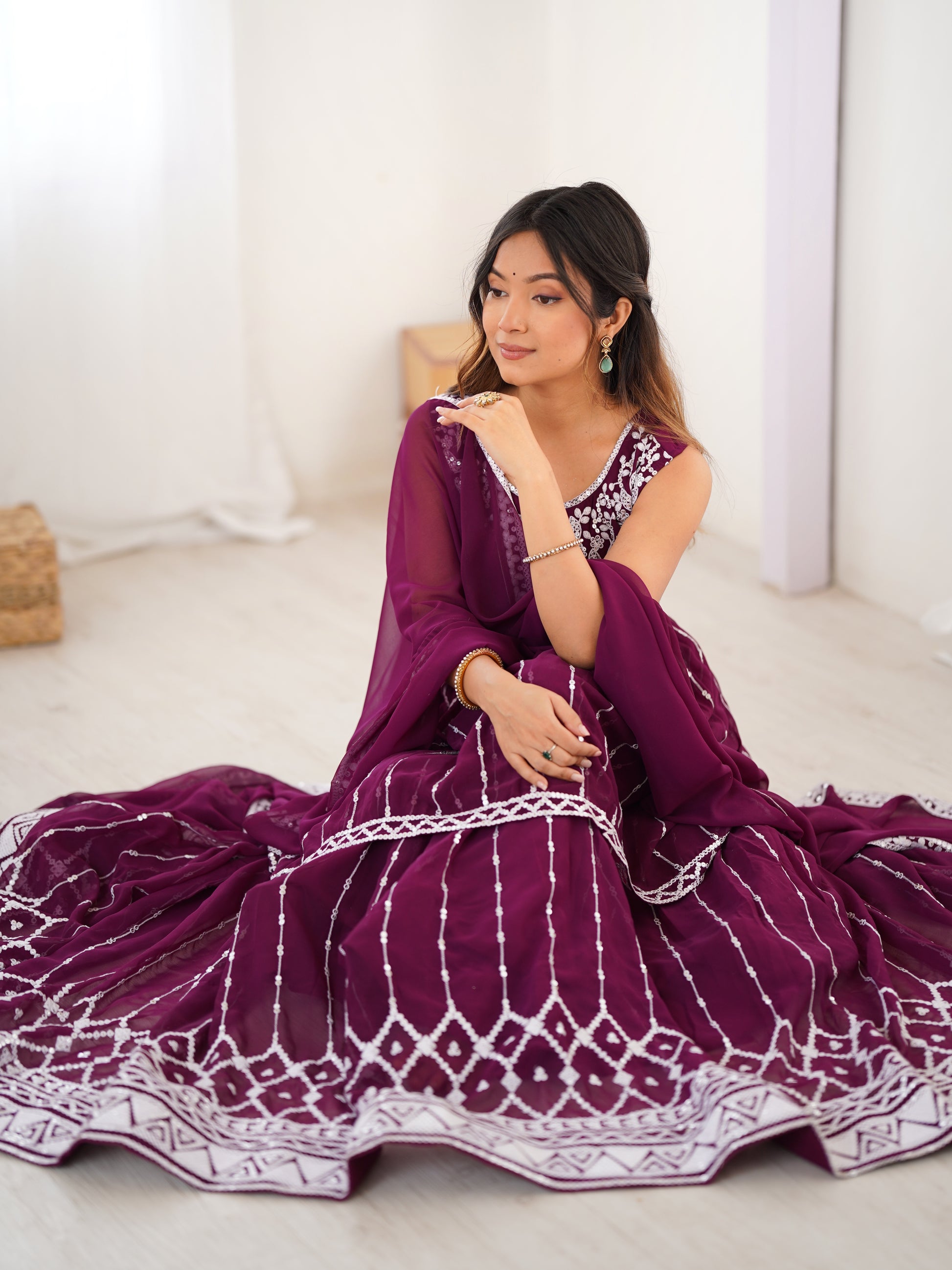 Woman wearing a purple saree with white patterns sitting on a white floor.