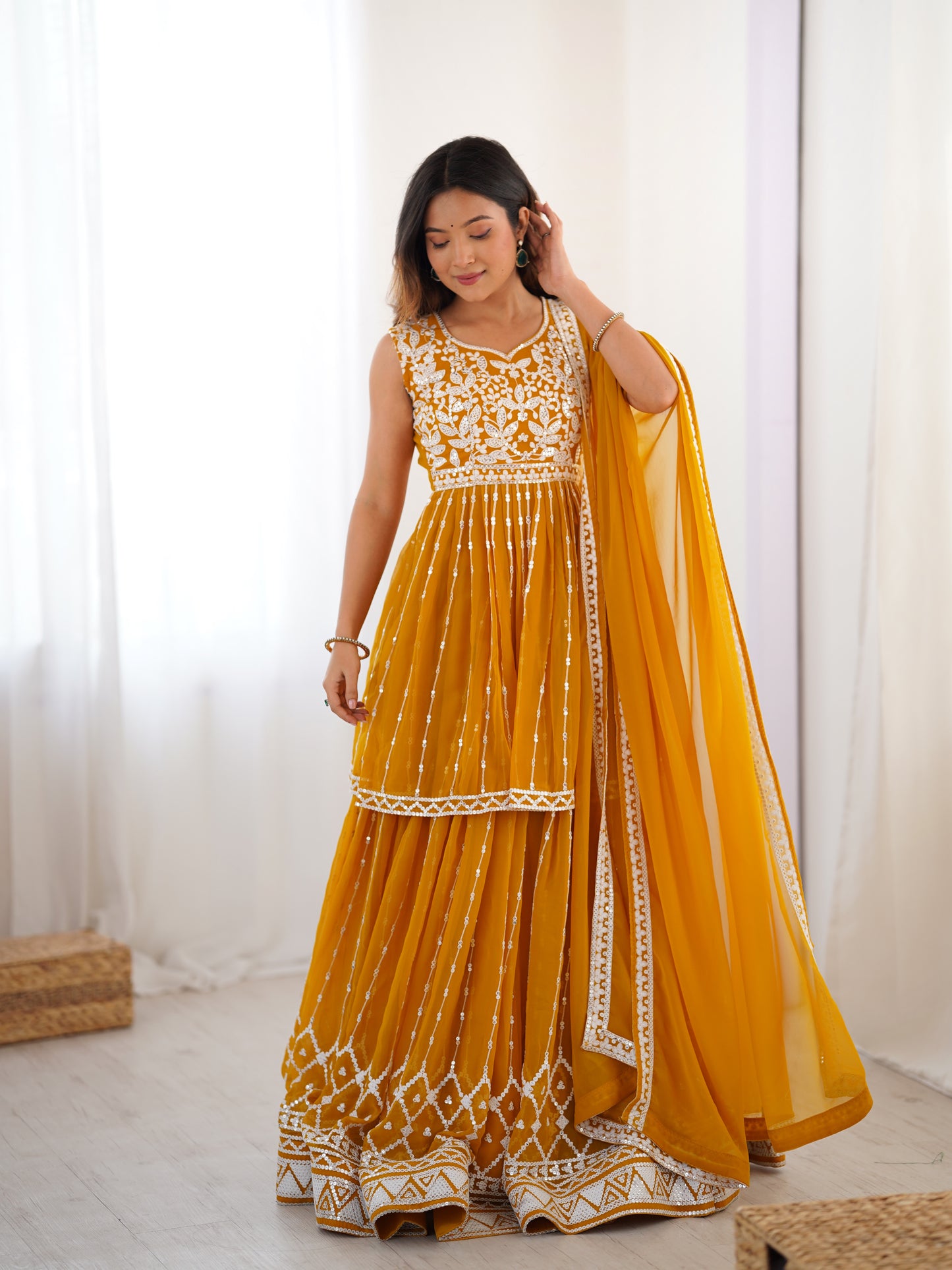 Woman wearing a yellow and white traditional outfit with a dupatta against a white background