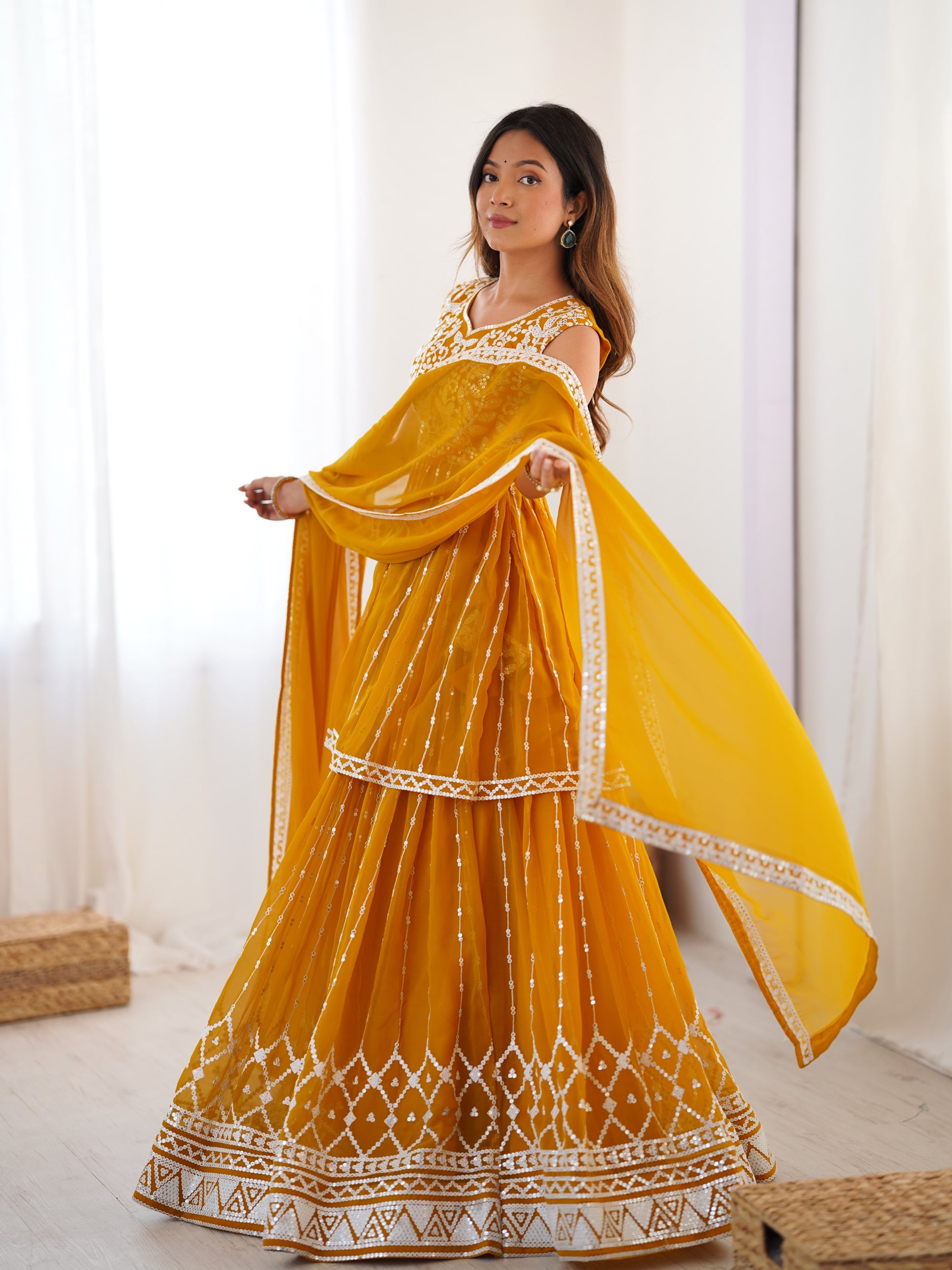 Woman wearing a yellow traditional outfit with white patterns indoors.