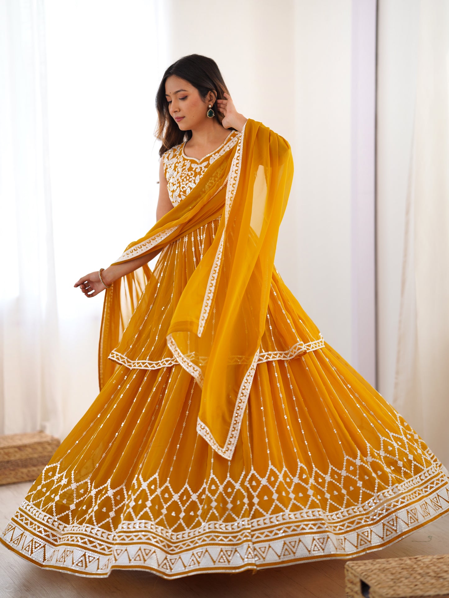 Woman wearing a yellow traditional outfit with white patterns indoors.