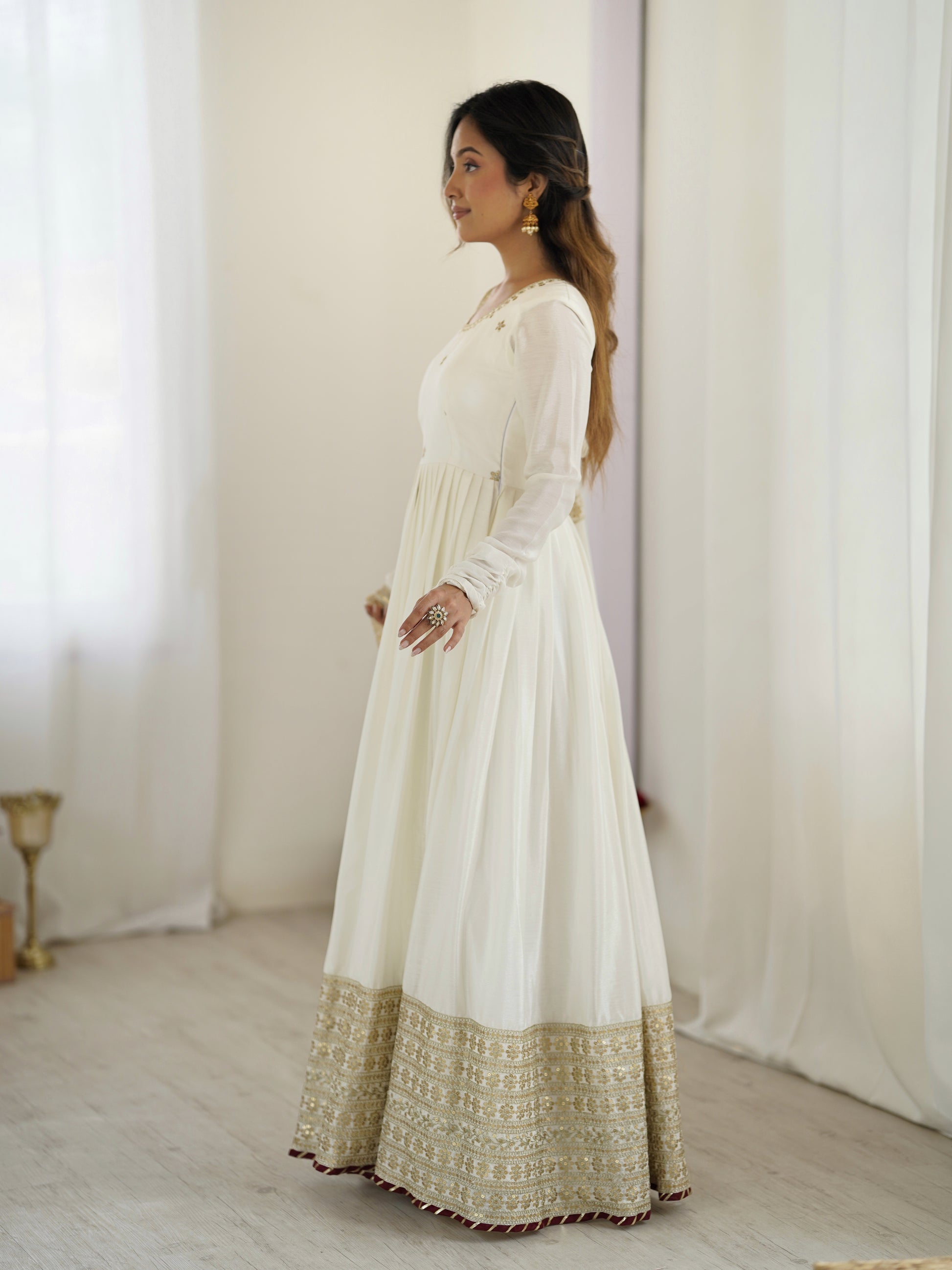 Woman wearing a white dress with gold trim against a white curtain background