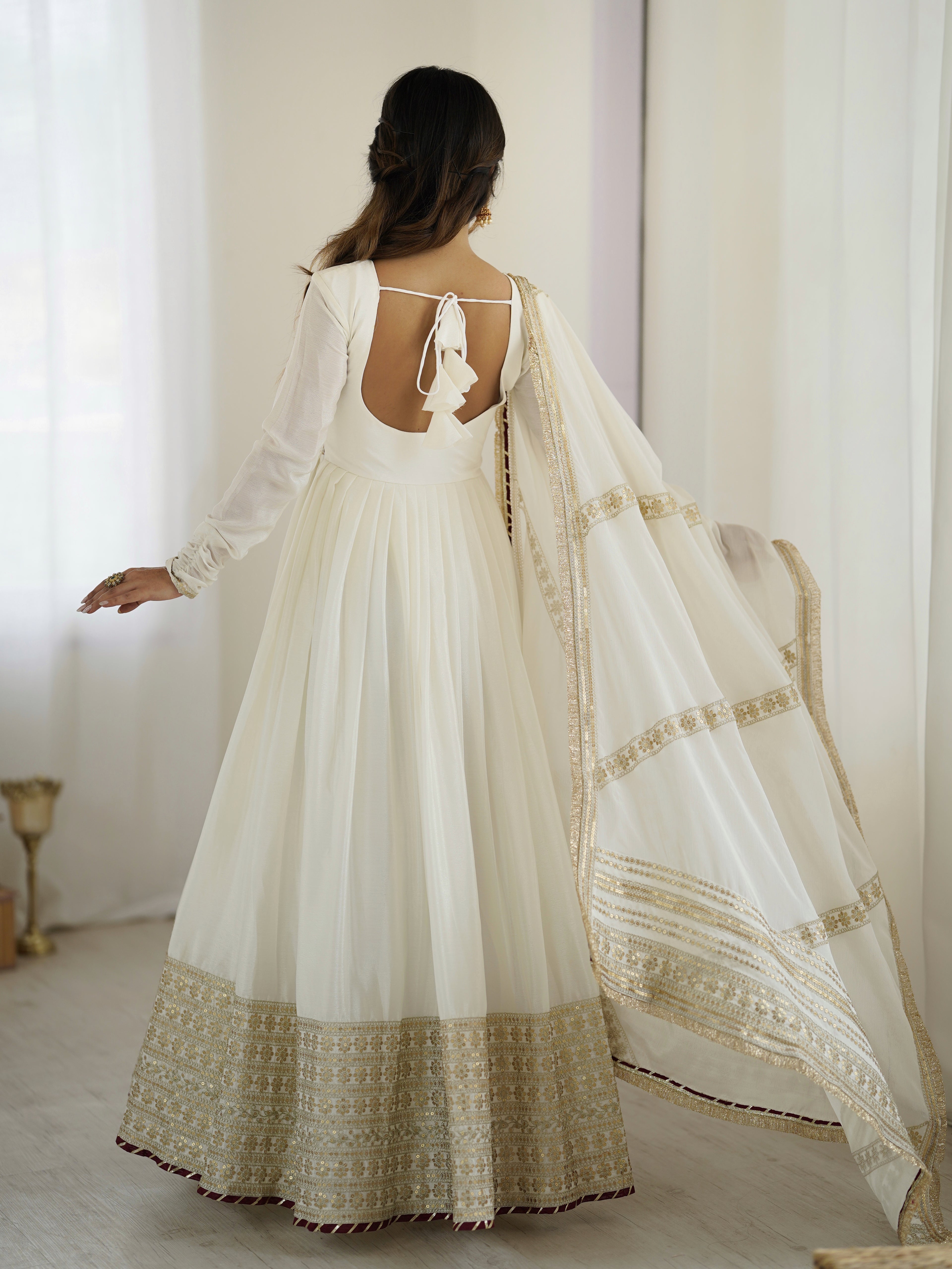 Woman wearing a white traditional outfit with gold details in a softly lit room.