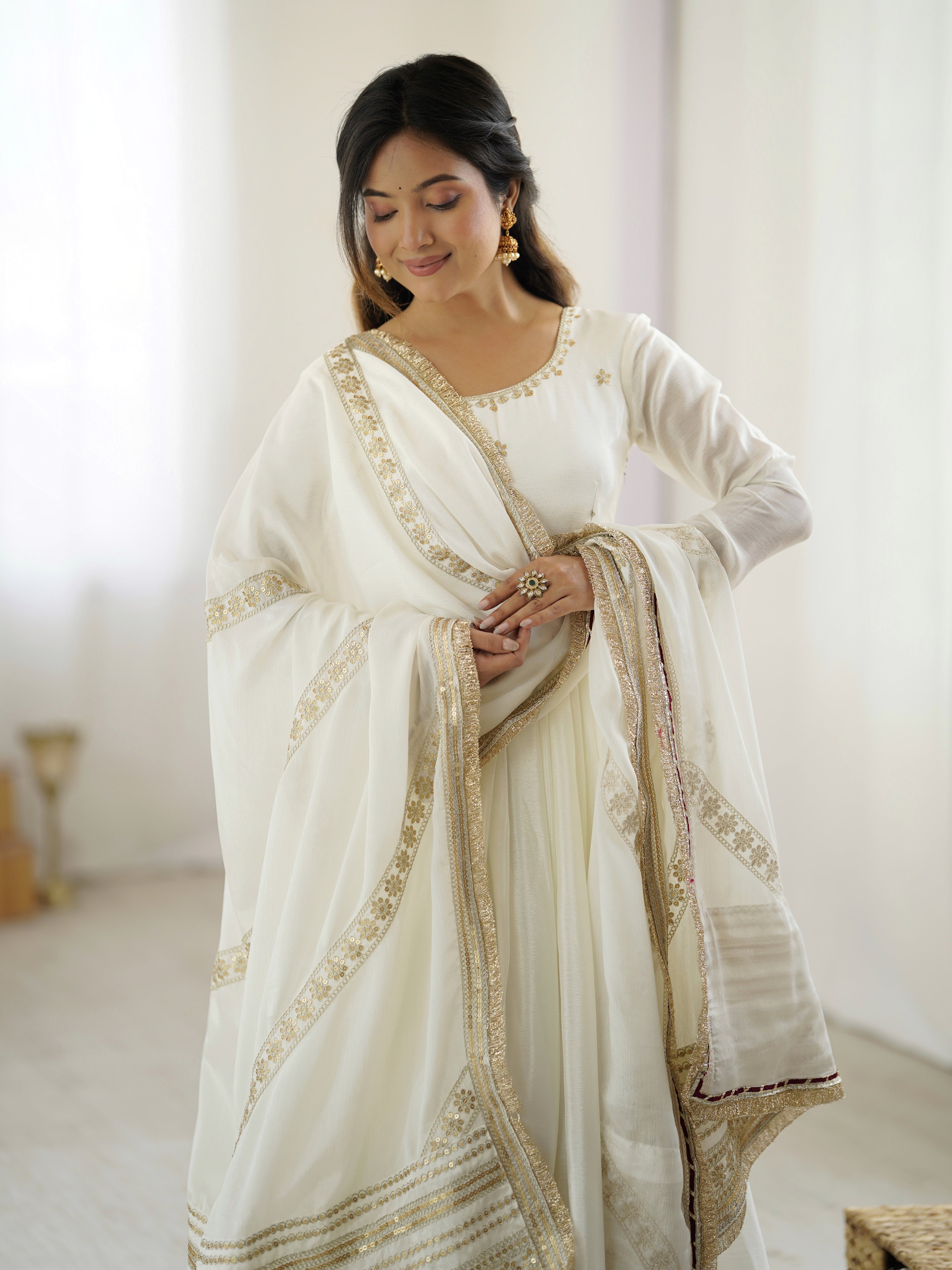 Woman wearing a white saree with gold embroidery in a minimalistic setting