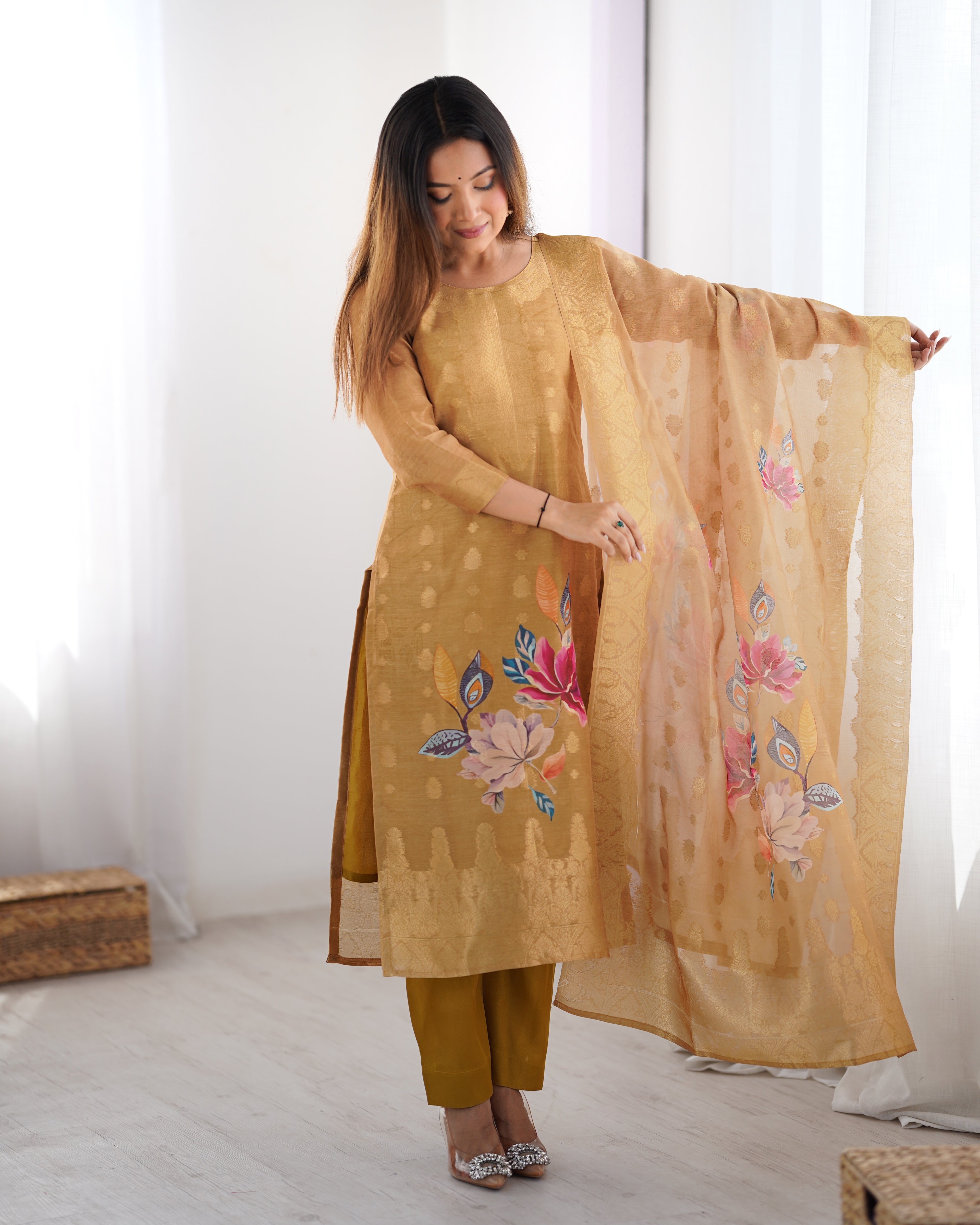 Woman wearing a mustard yellow traditional outfit with floral embroidery in a bright room.
