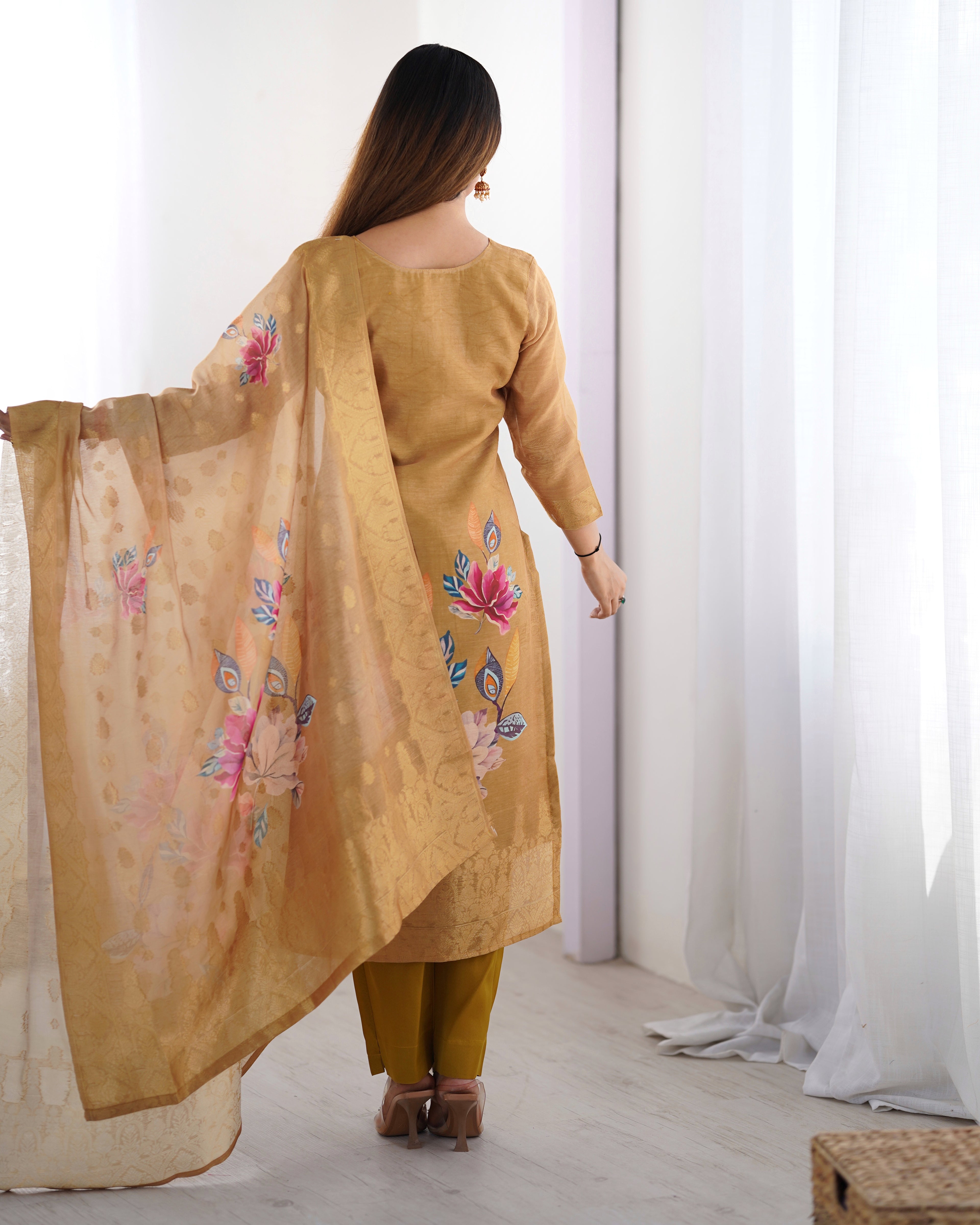 Woman wearing a mustard yellow kurta with floral embroidery, standing in a room with white curtains.
