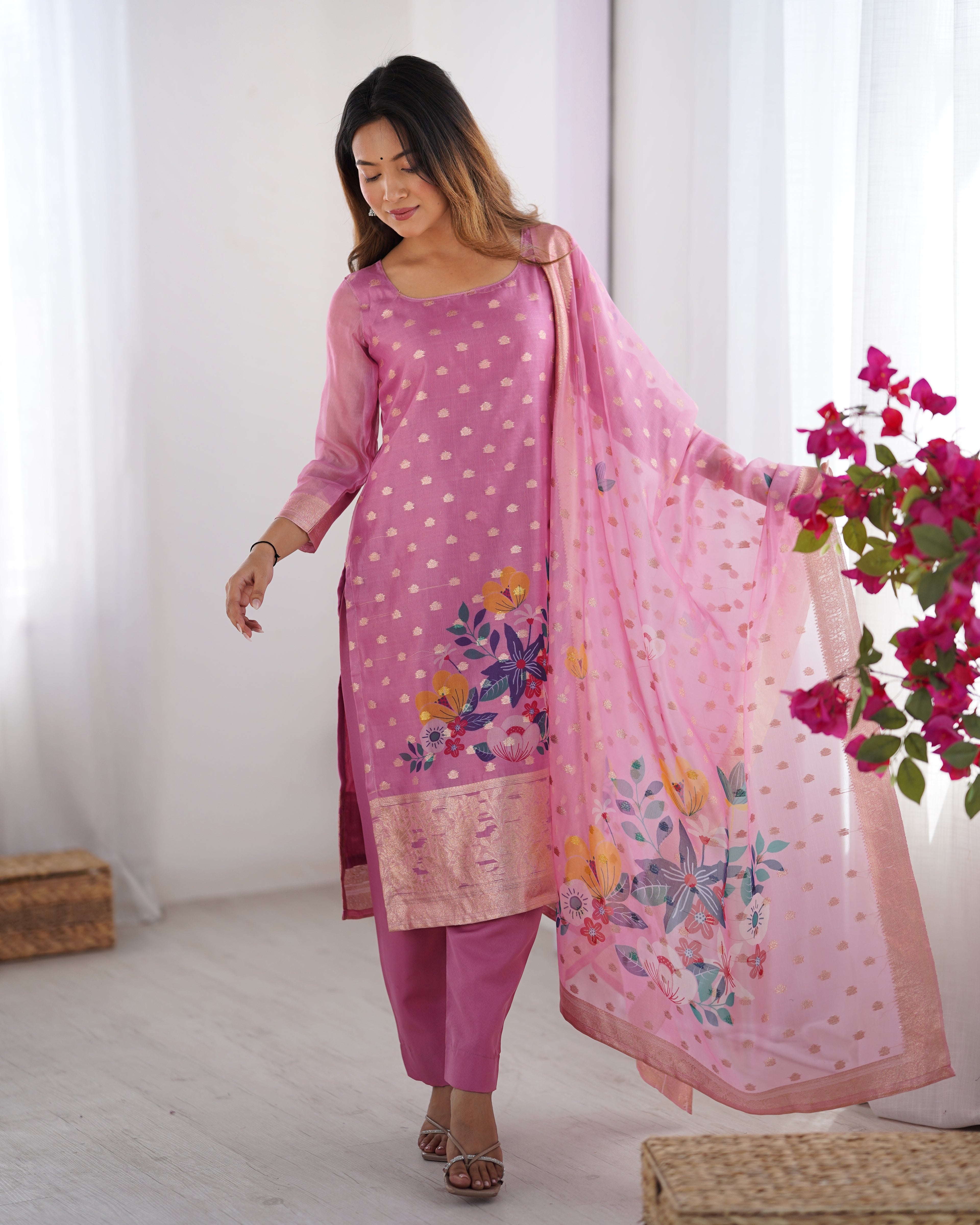 Woman wearing a pink traditional outfit with floral patterns in a bright room.
