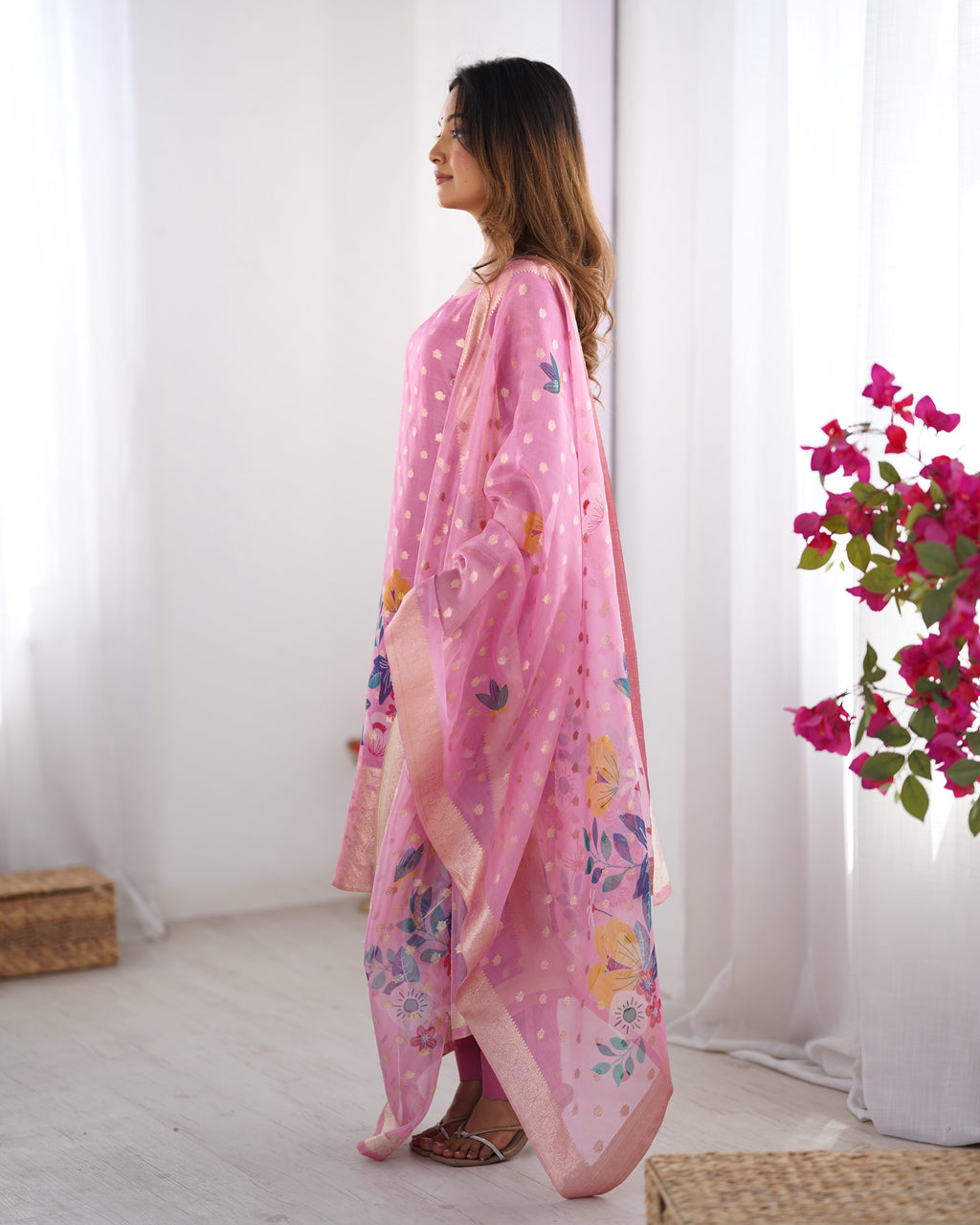 Woman wearing a pink floral dress with a matching dupatta in a minimalistic room.