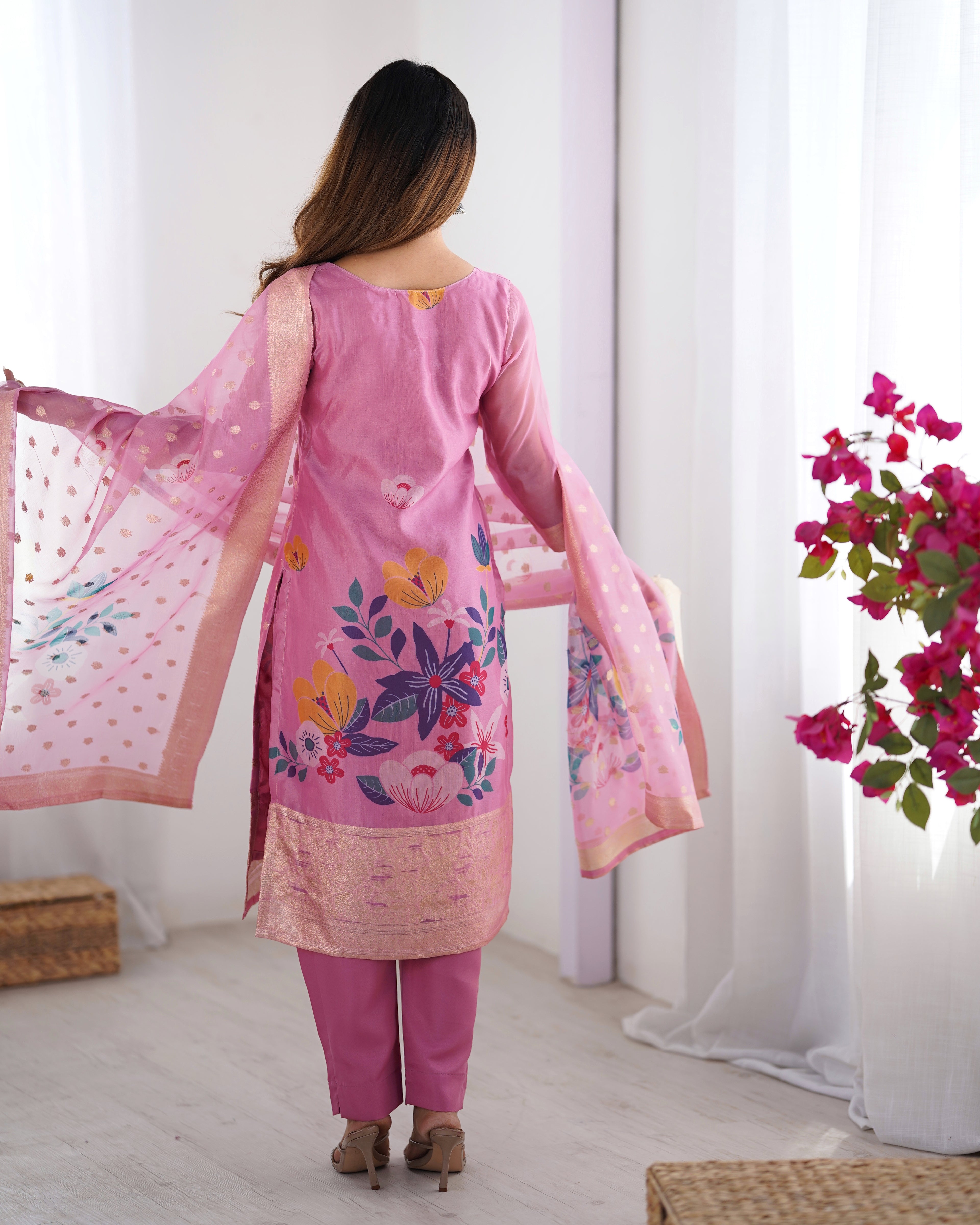 Woman wearing a pink floral dress with a matching dupatta in a bright room.