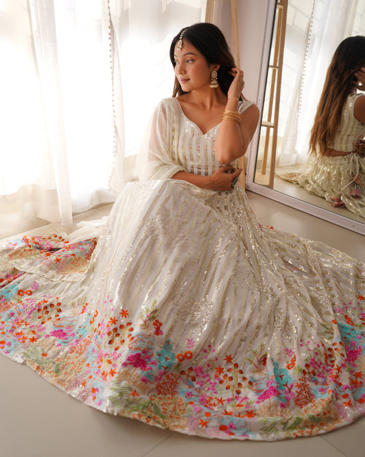 Woman in a white saree with floral patterns sitting on the floor.
