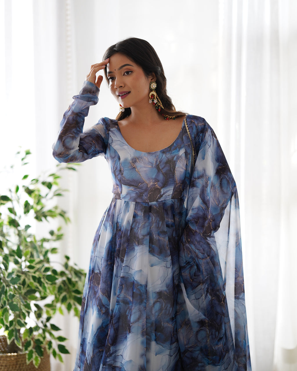 Woman wearing a blue floral dress with sheer sleeves in a bright room.