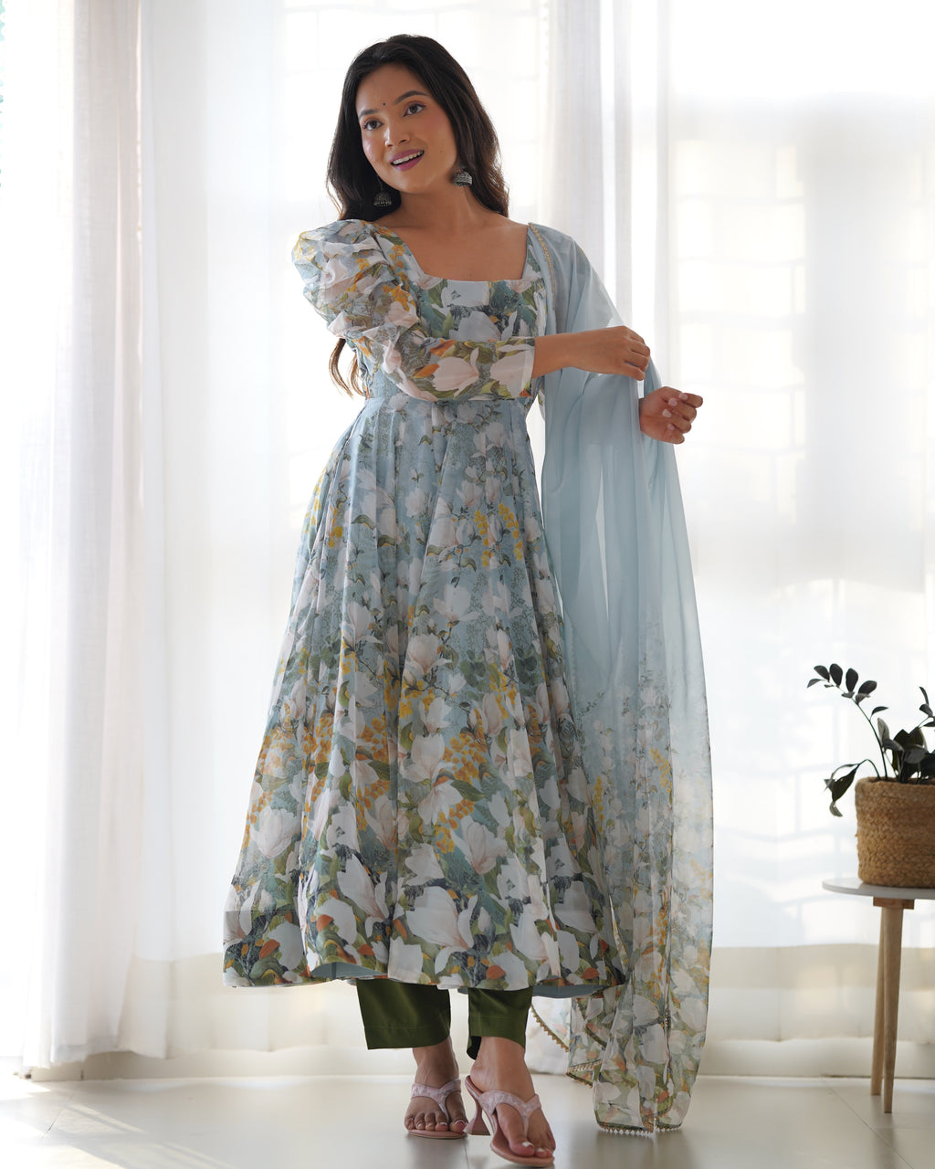 Woman wearing a floral dress with a sheer dupatta in a bright room.