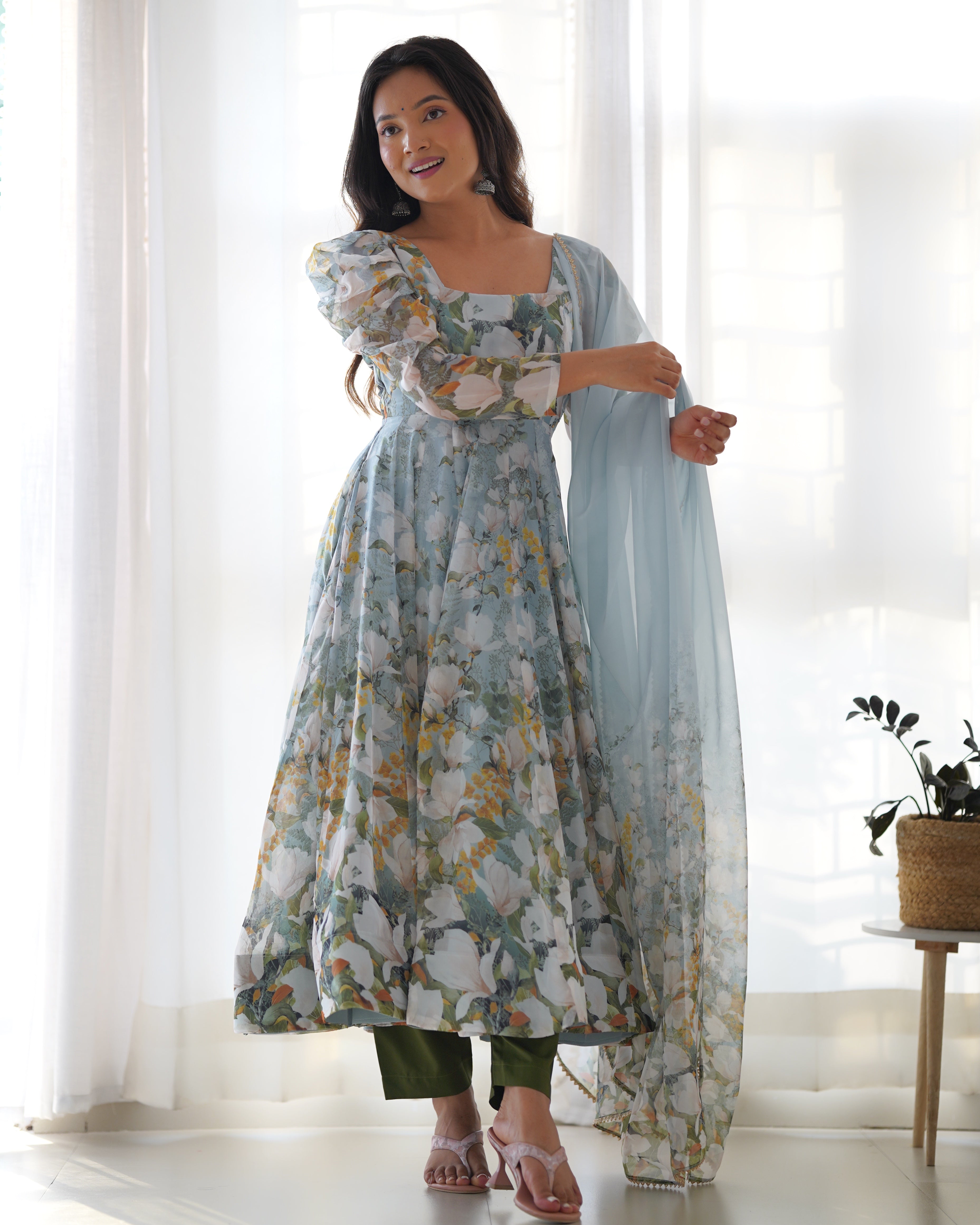 Woman wearing a floral dress with a sheer dupatta in a bright room.