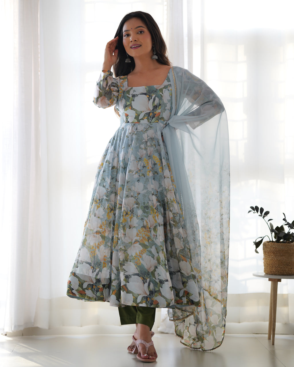 Woman wearing a floral dress with a sheer dupatta in a bright room.